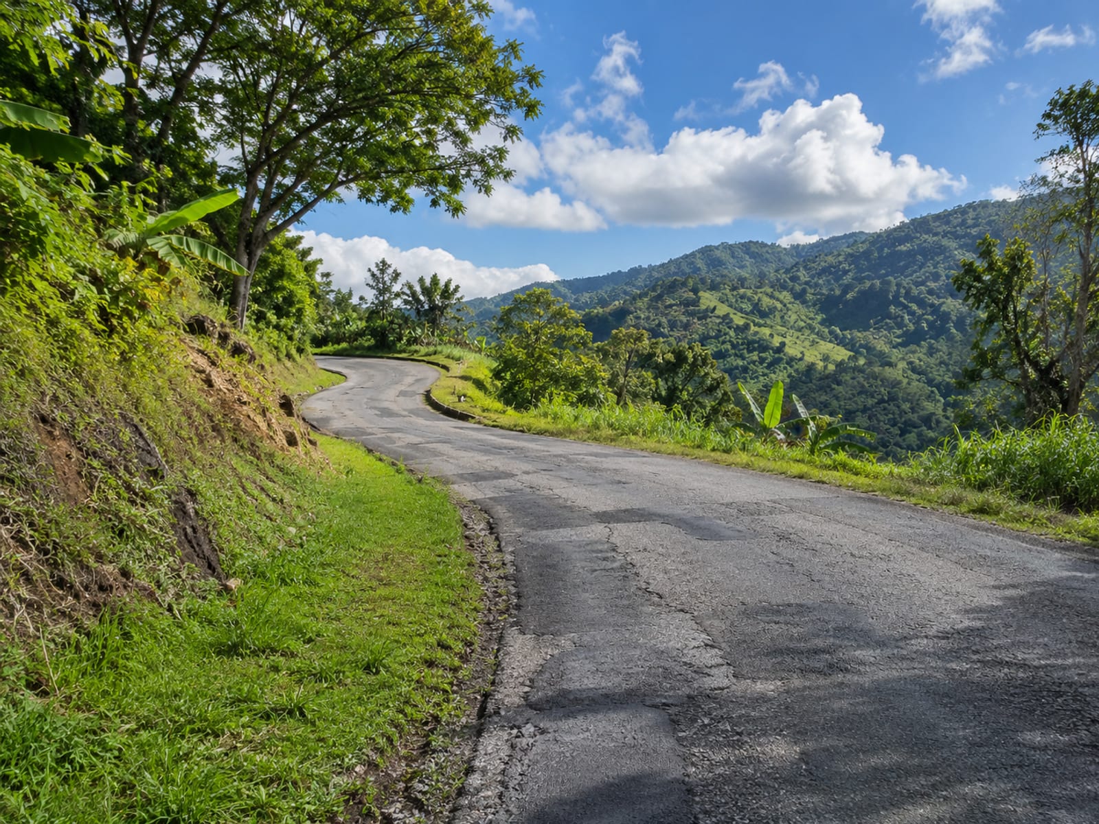 A winding rural road climbing through green hills under a bright sky