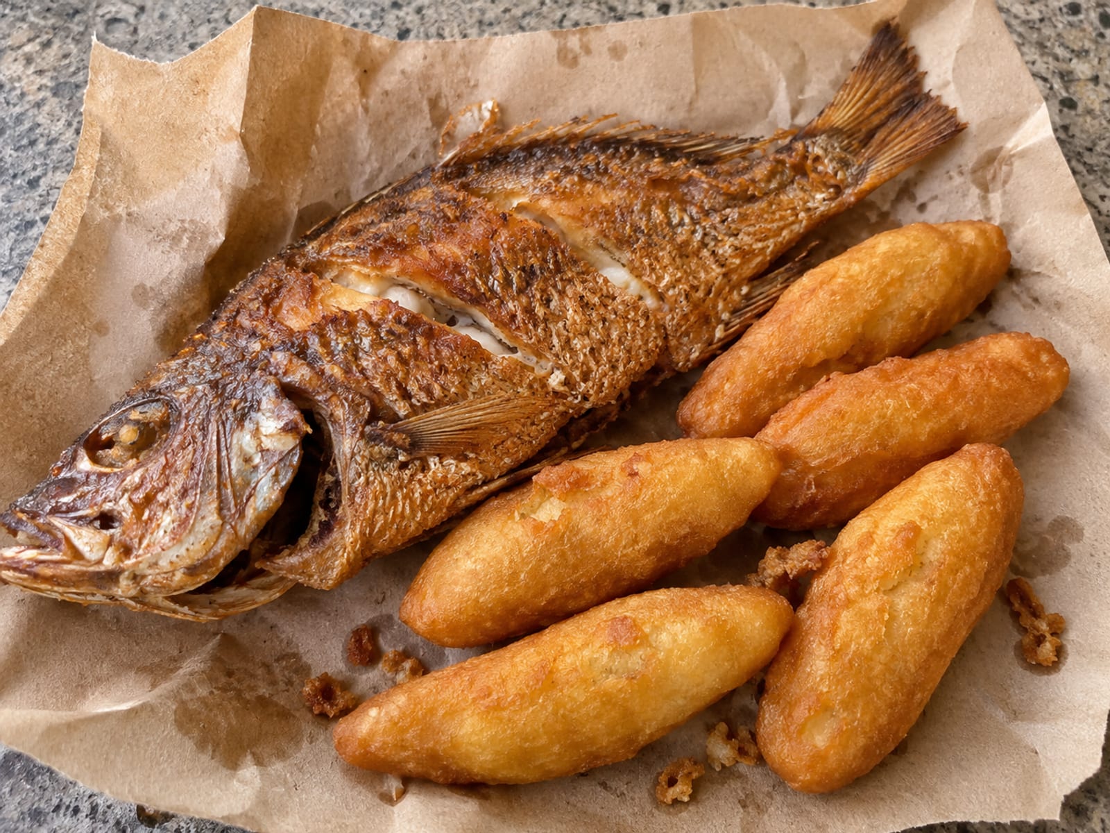 Whole fried fish and festival wrapped in paper on a plain street-side counter