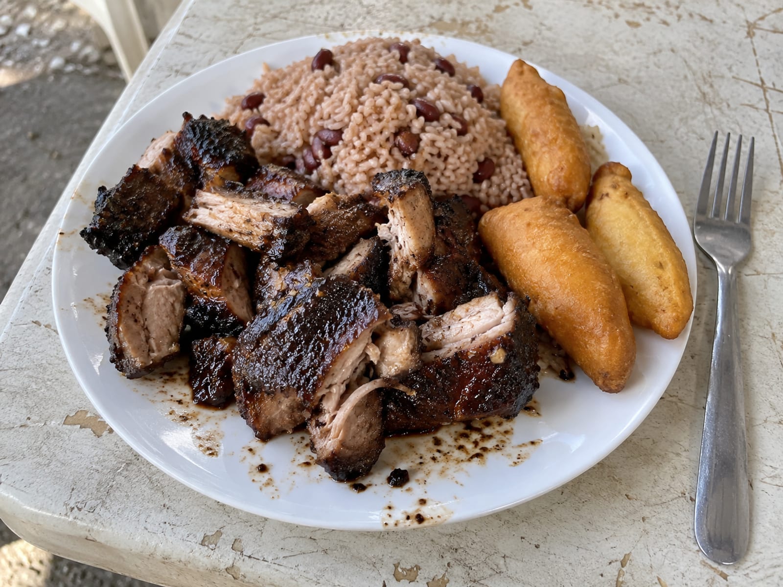 Jerk pork with rice and peas and fried festival on a simple plate