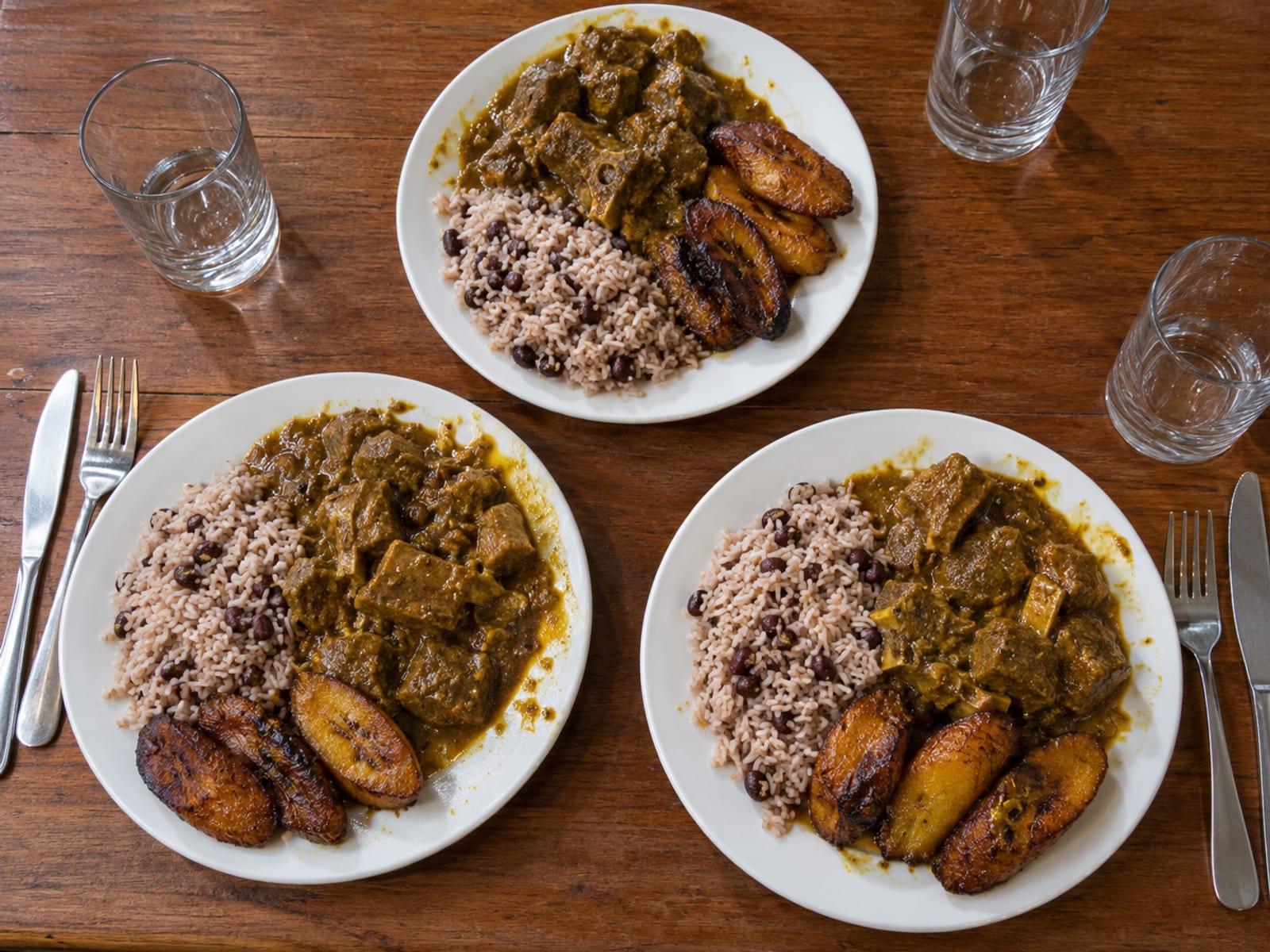 Plates of curried goat, rice and peas and plantain on a restaurant table