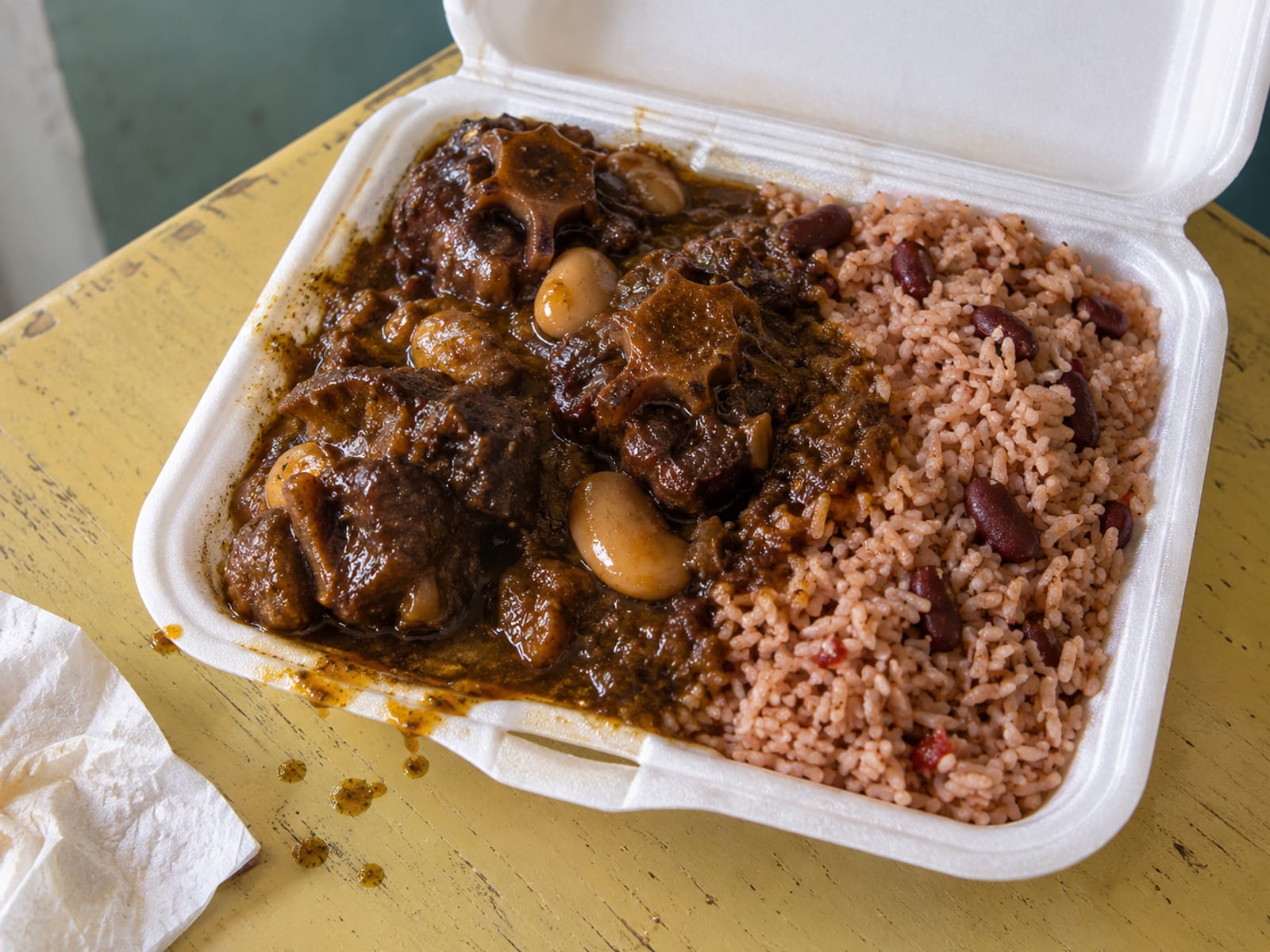 A foam takeaway box of oxtail with rice and peas and gravy