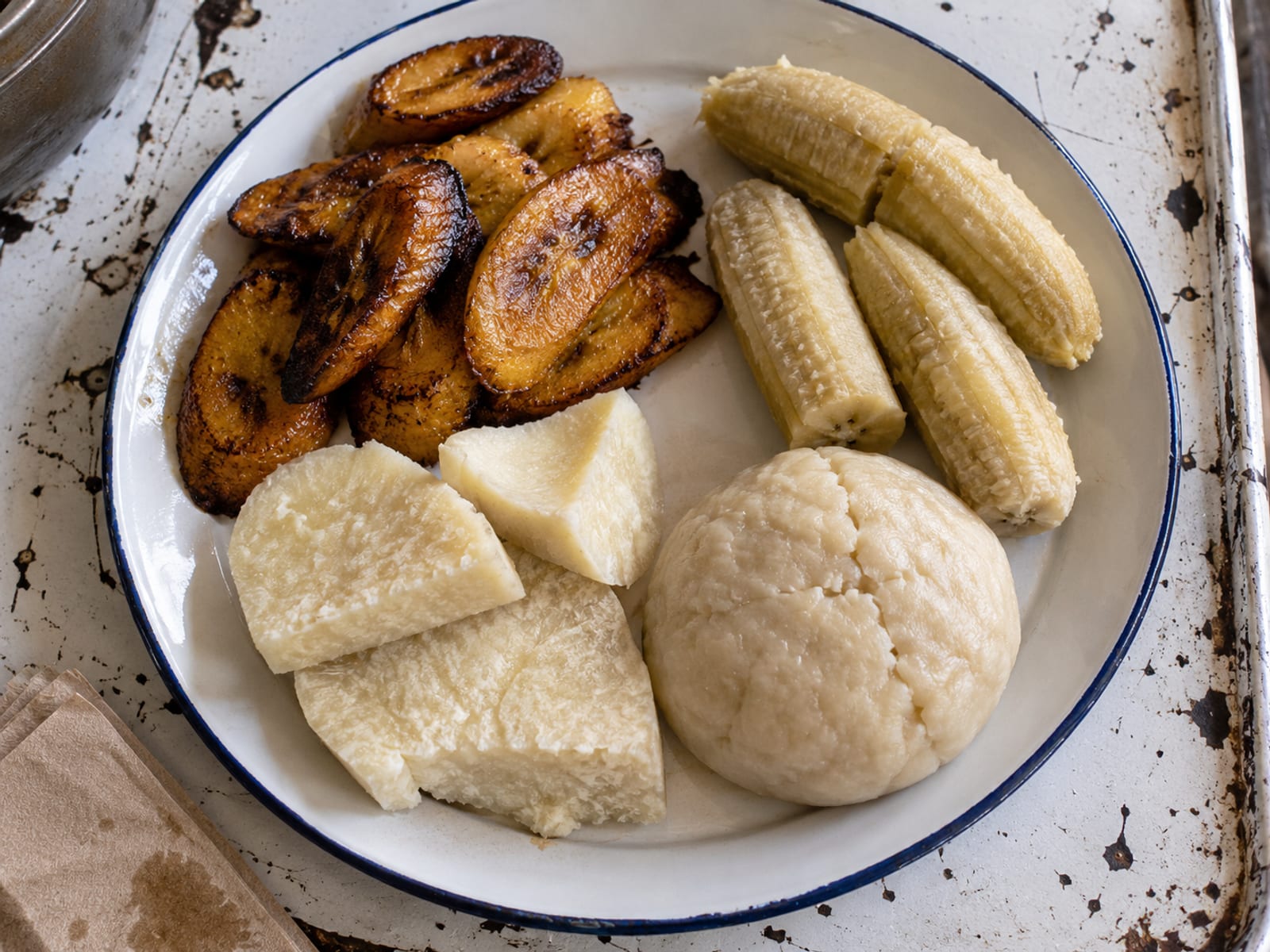 Fried plantain, boiled green banana, yam and a dumpling arranged on a plate