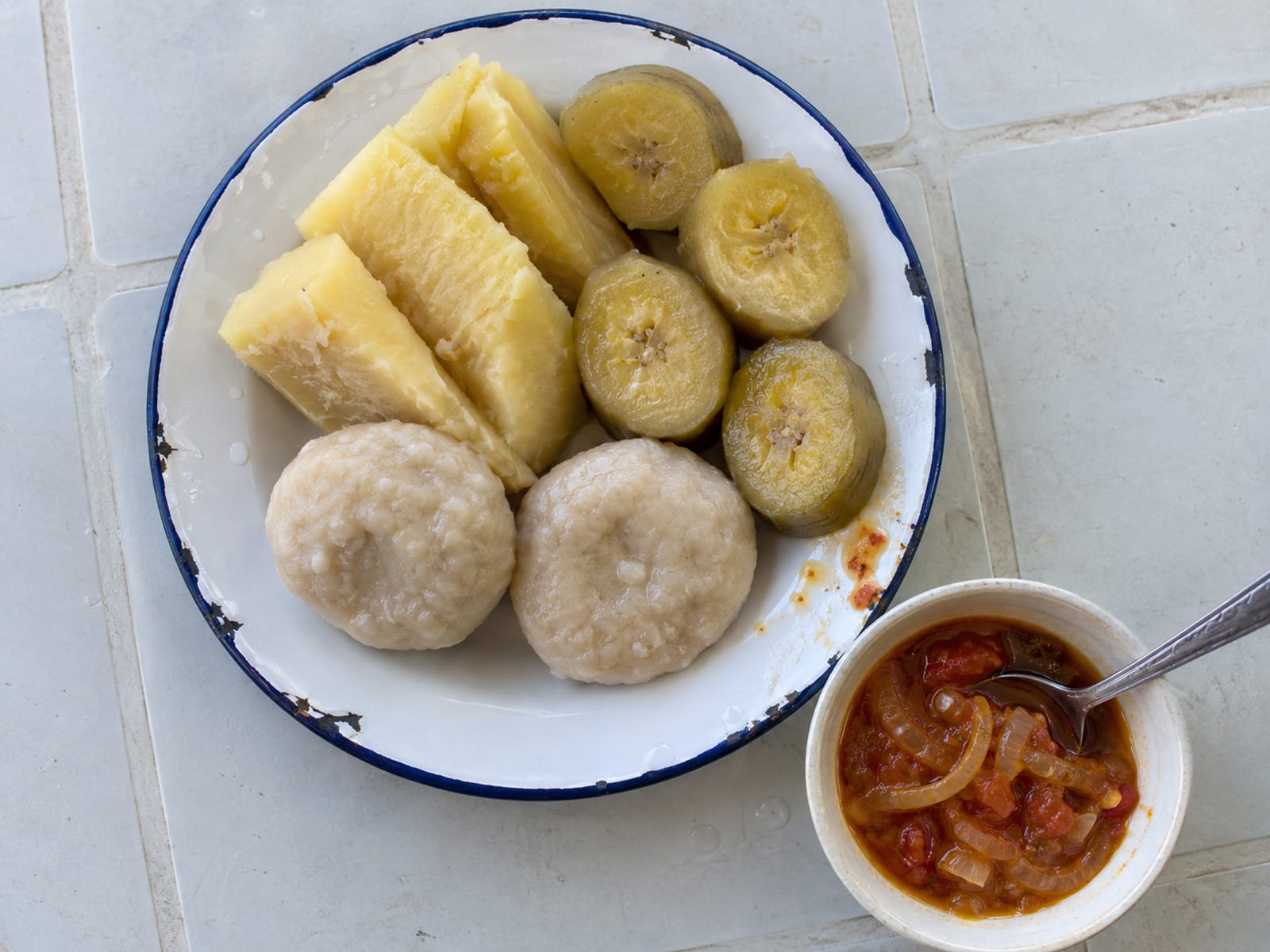 Boiled yam, green banana and dumplings on a plate beside a small bowl