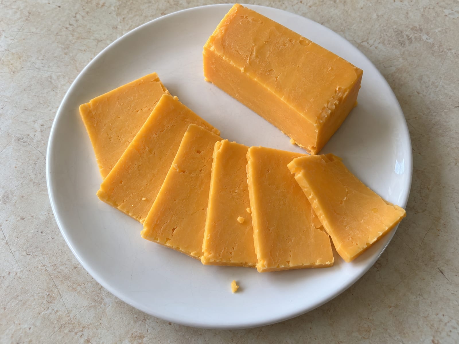 Slices of soft pale orange cheddar-style cheese fanned on a white plate