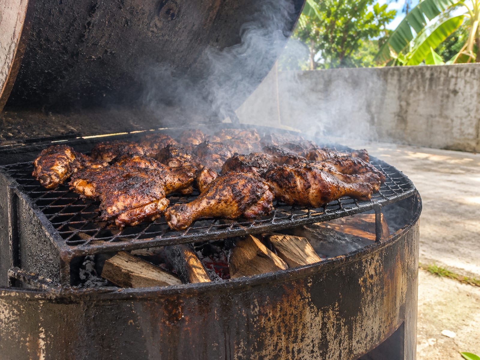Jerk chicken pieces grilling over smoke on an open metal drum