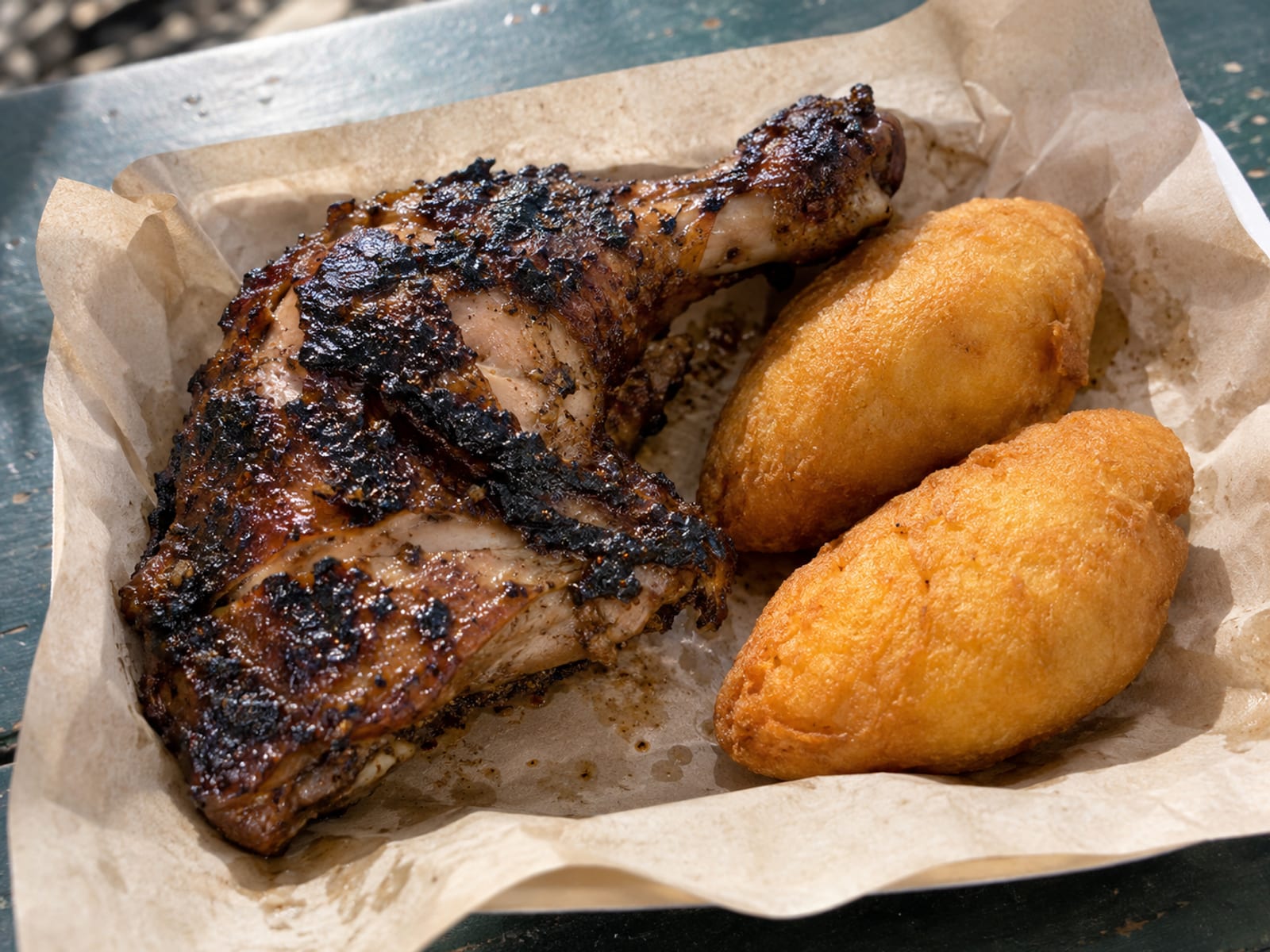 A quarter jerk chicken with festival on a paper-lined tray
