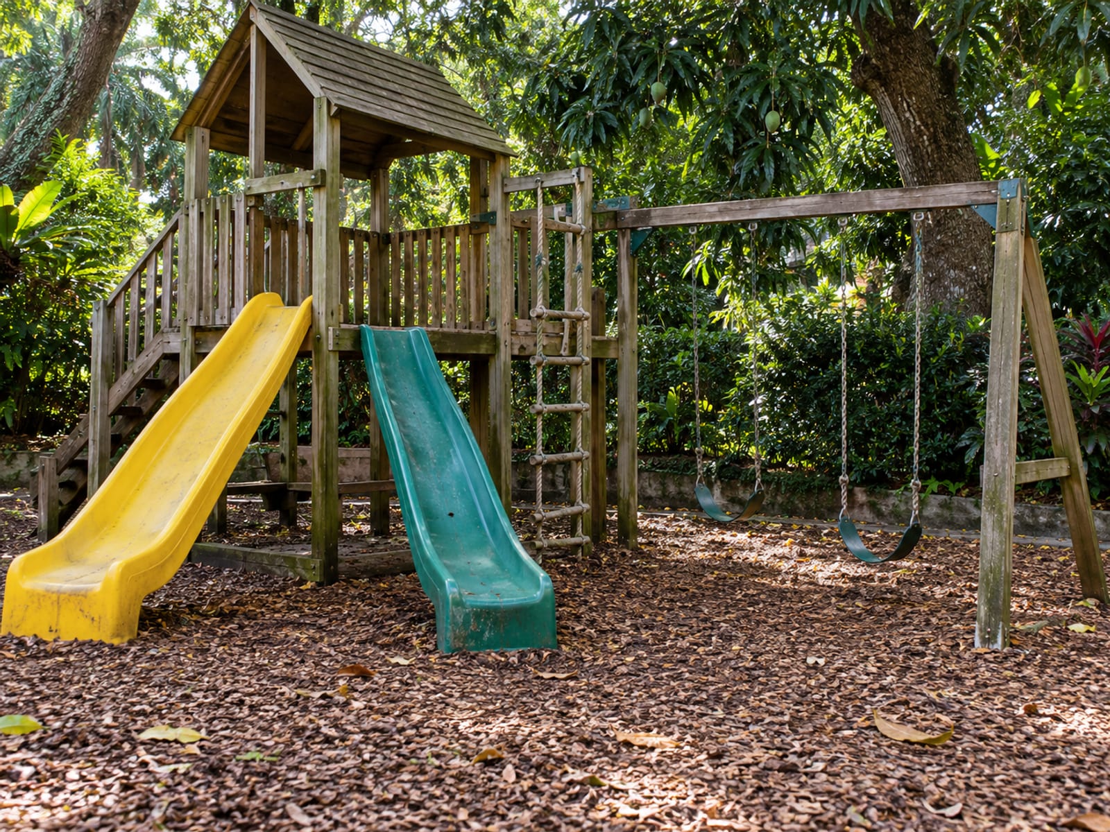 Playground slides and swings in a shaded green garden, empty in morning light