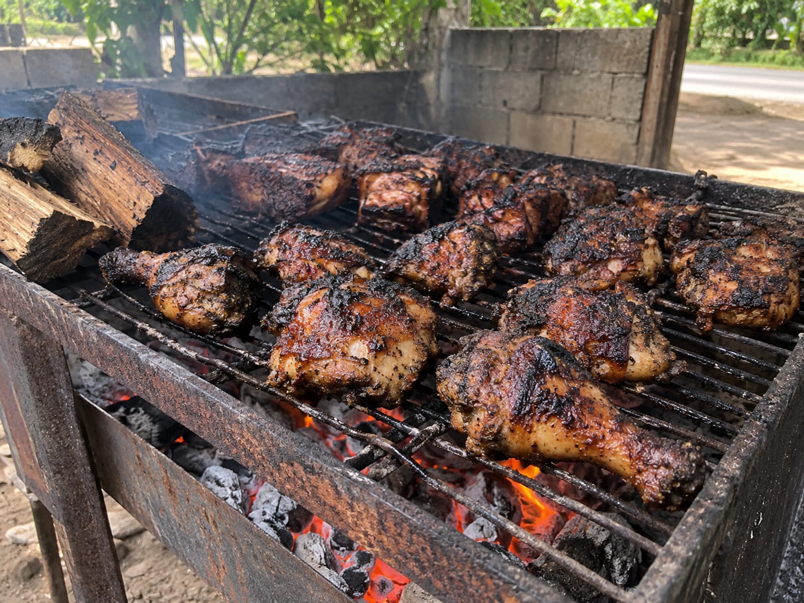 Jerk chicken and pork pieces on a metal grill over glowing coals