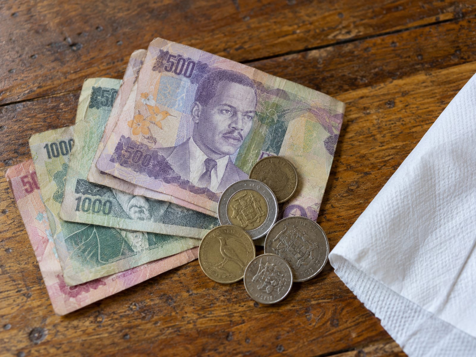 Stack of Jamaican banknotes and a few coins beside a folded paper napkin