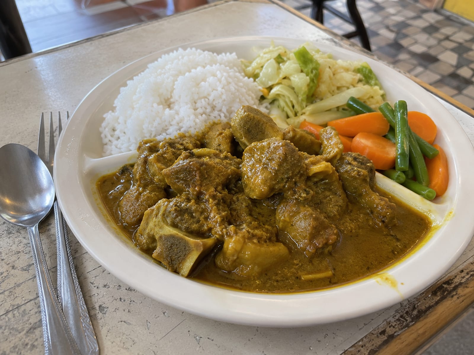 A plate of curry goat with white rice and steamed vegetables