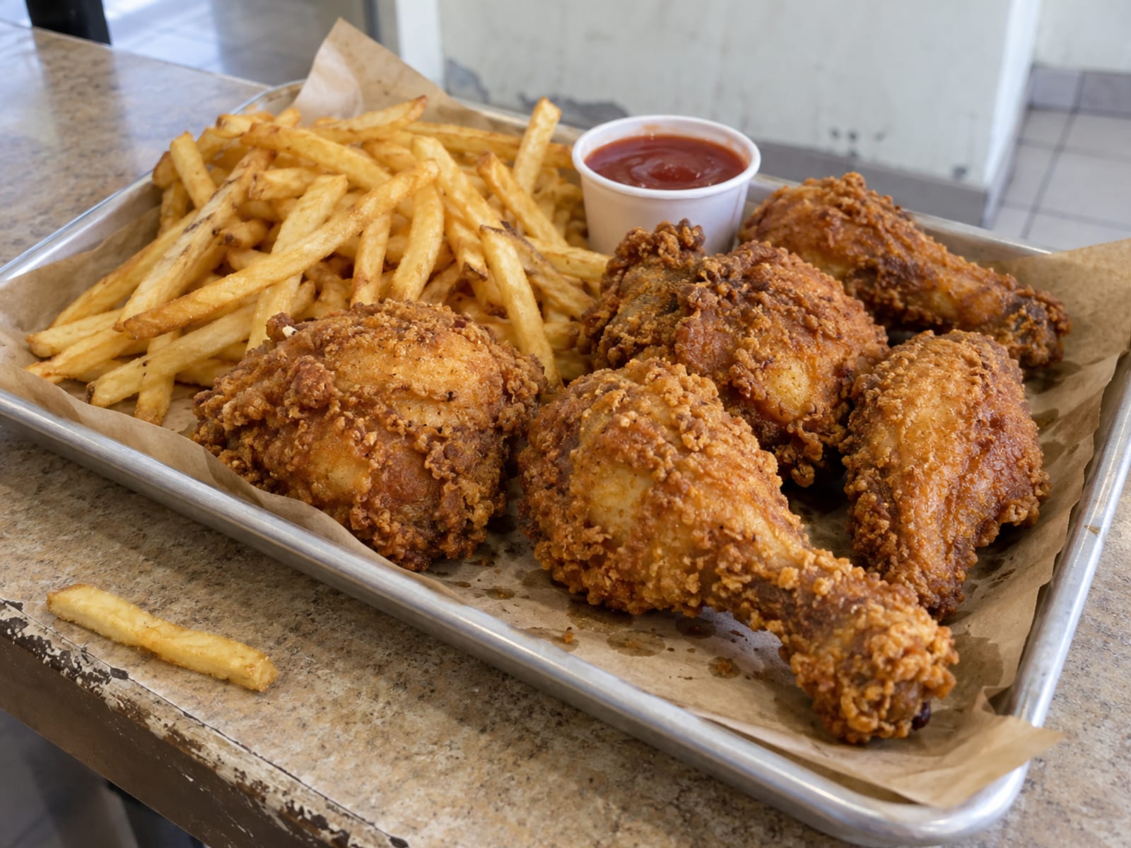 A plain tray of golden fried chicken pieces with fries on a counter