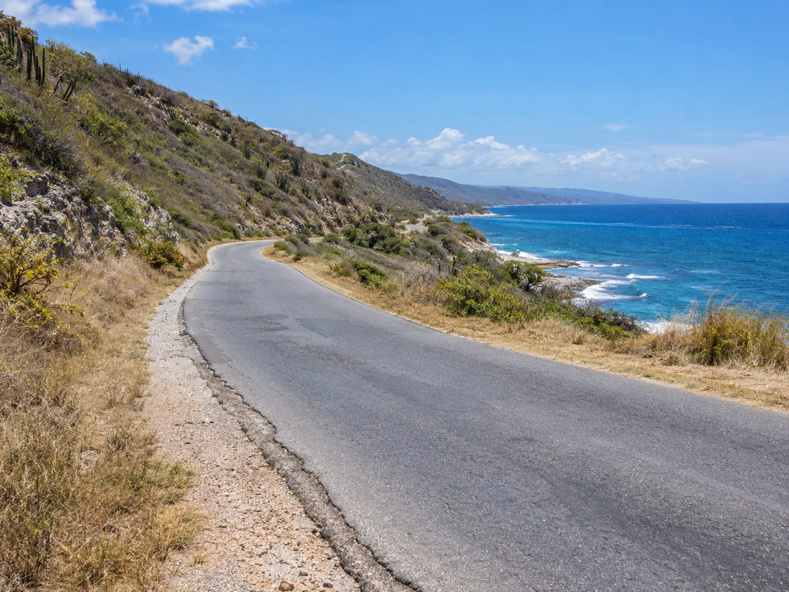 A coastal road with low scrub hills on one side and the sea on the other