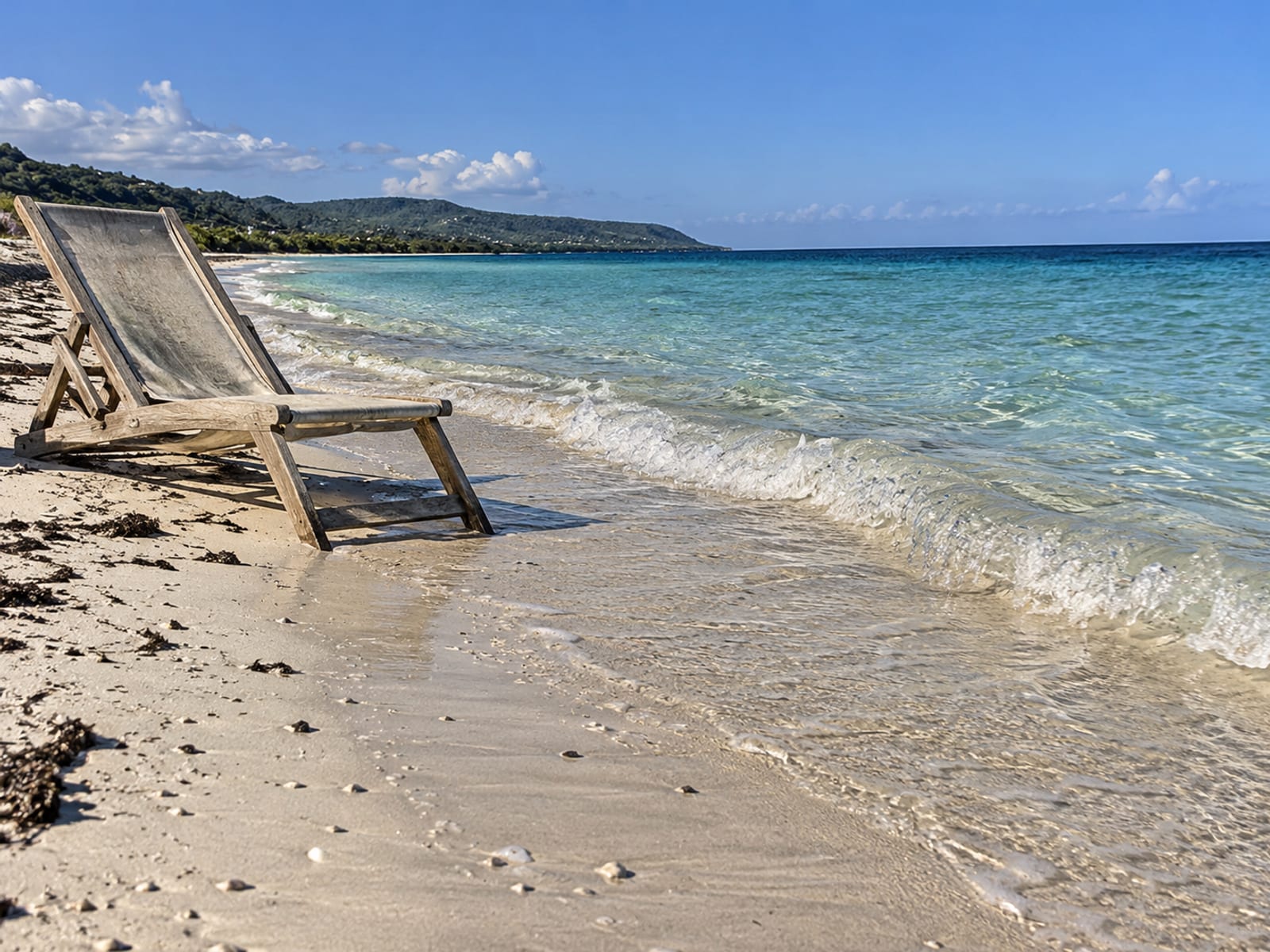 Clear shallow turquoise water over pale sand with a lounge chair on the shore