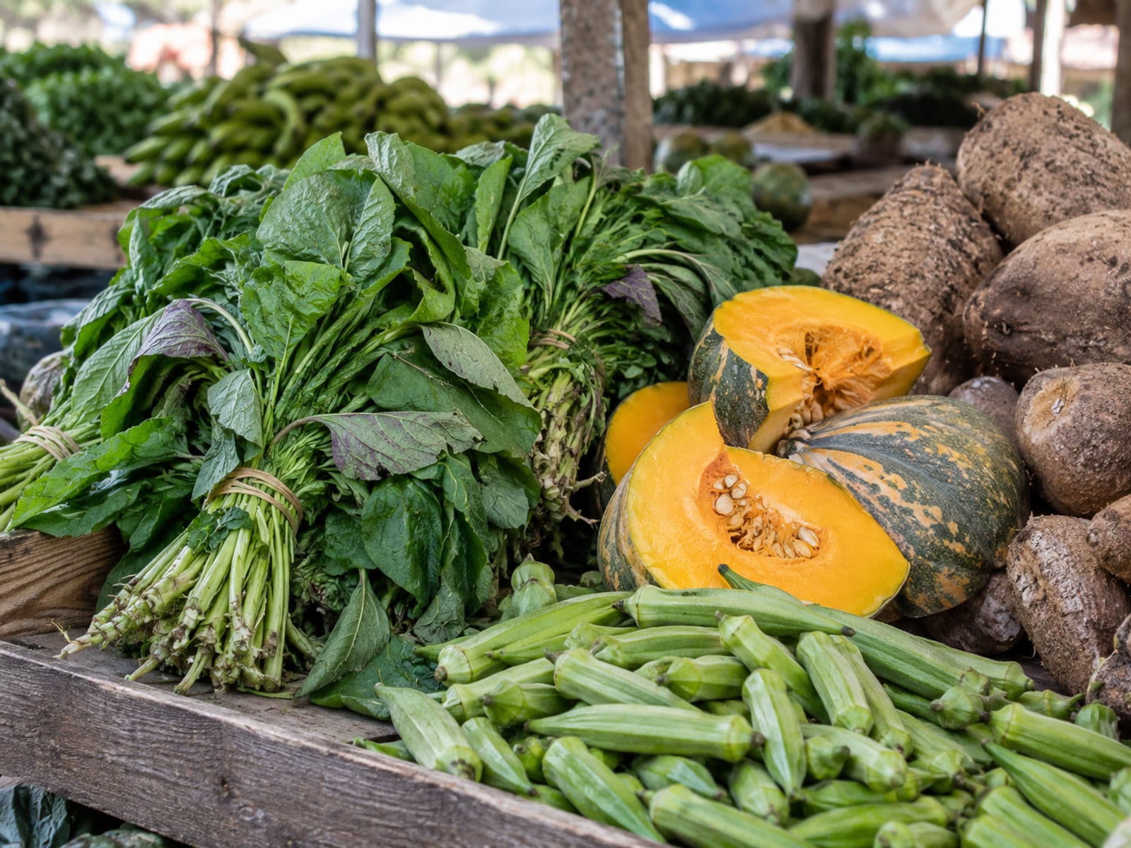 Fresh callaloo, pumpkin, okra and ground provisions piled on a market table