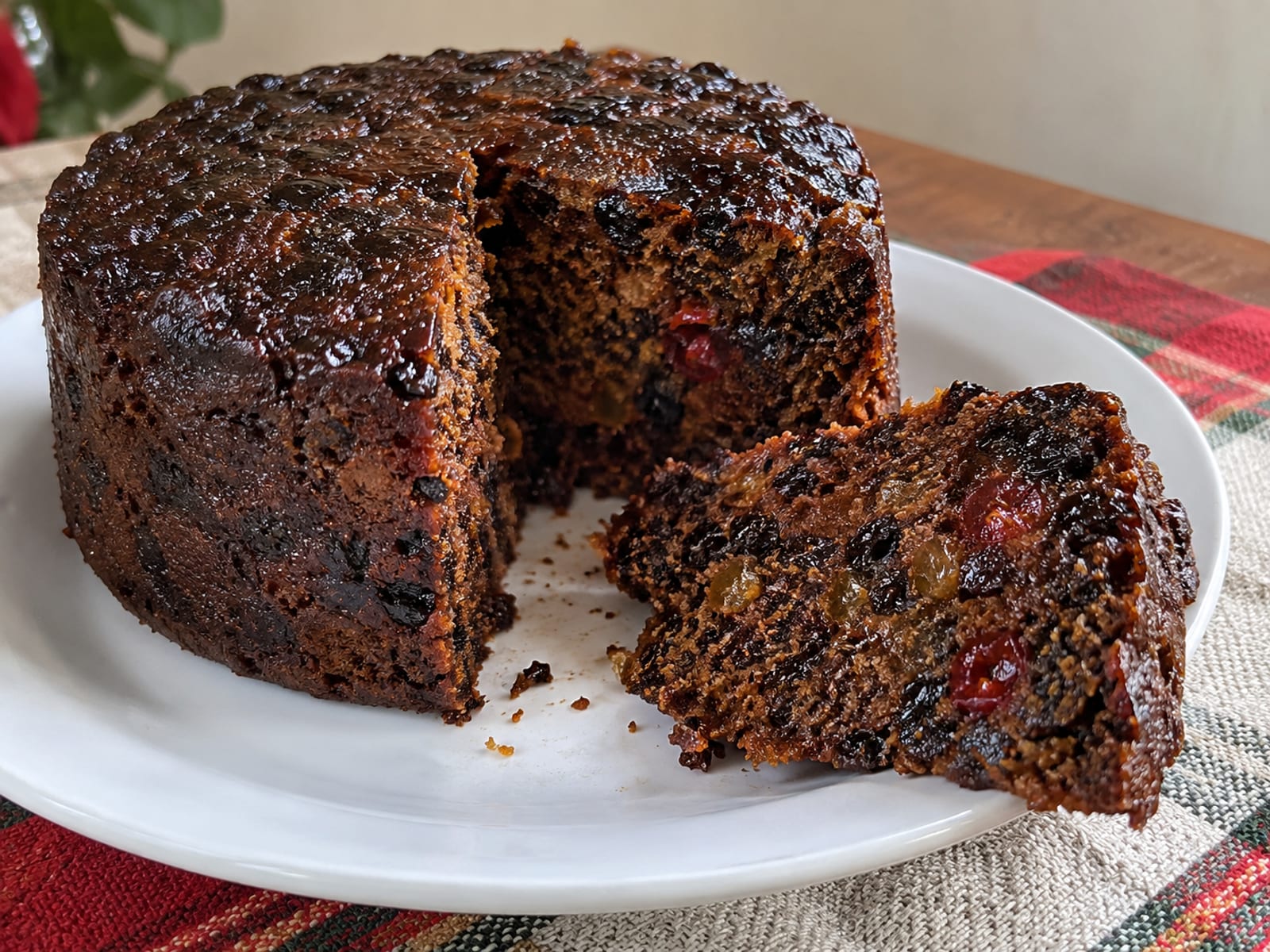 A dark, rich fruit cake with a slice cut away on a plain plate