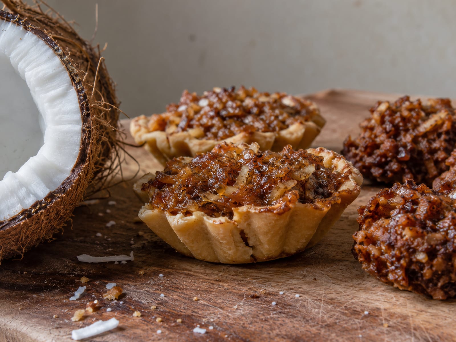 Gizzada and coconut drops arranged on a plain wooden board beside a halved coconut