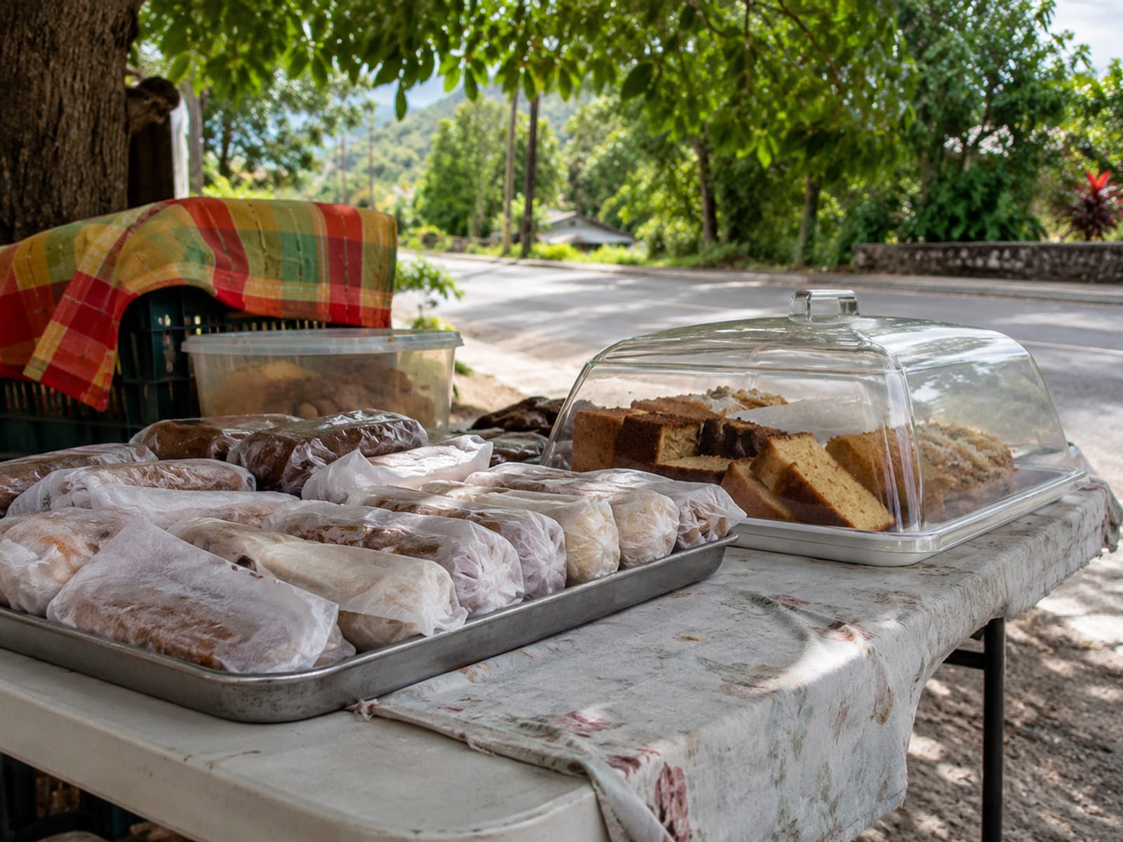 A roadside table with a tray of wrapped sweets and baked goods in the shade