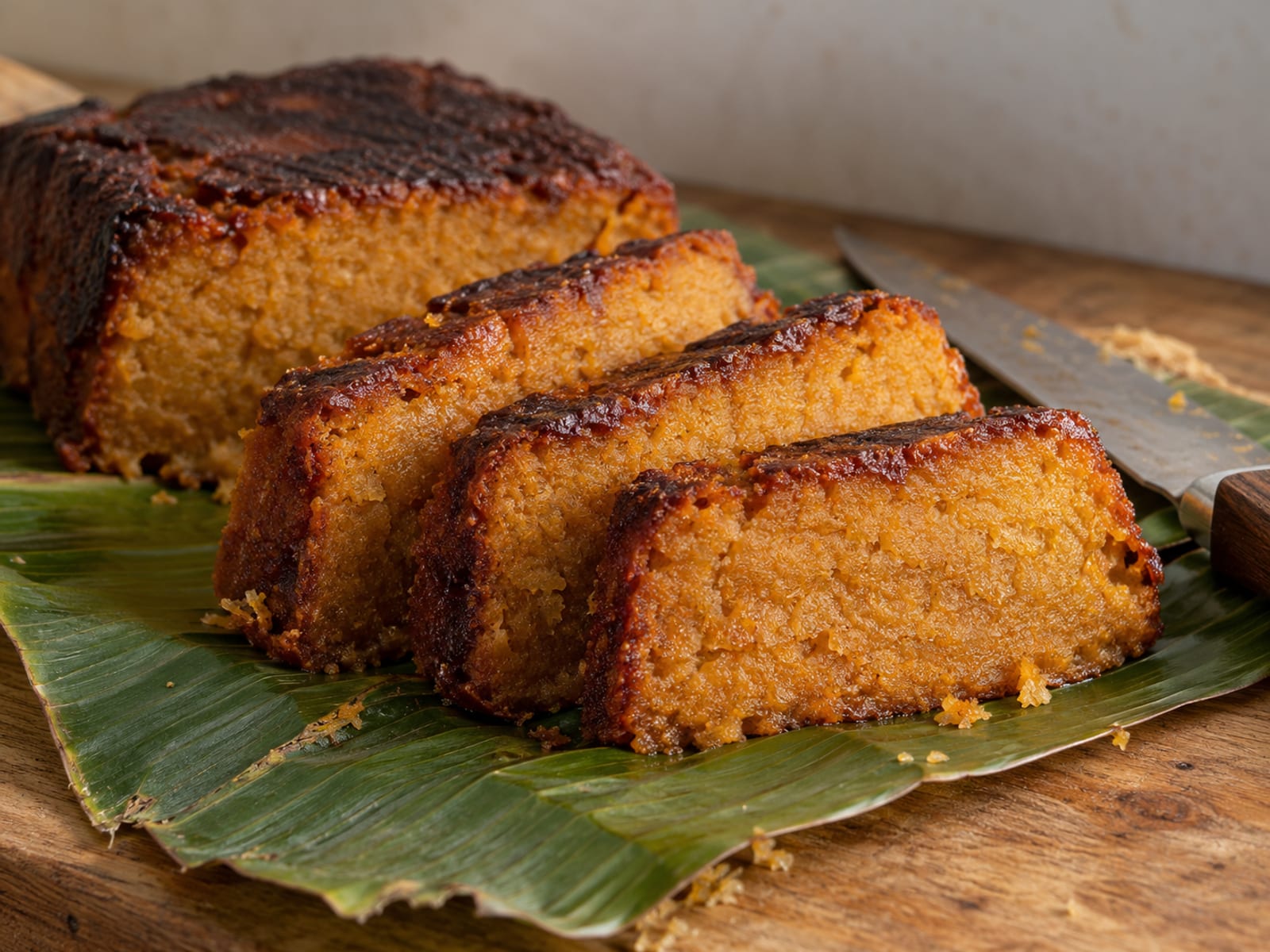 A golden-brown sweet potato pudding cut into slices on a banana leaf