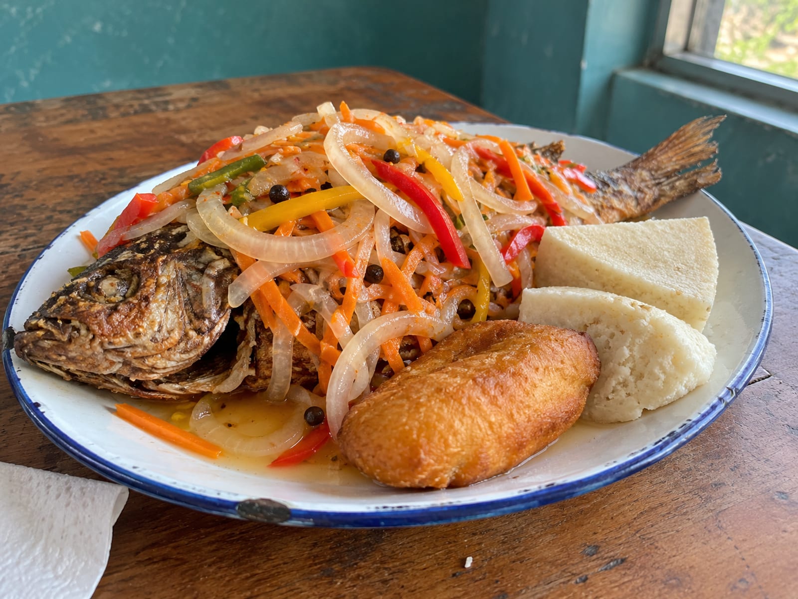 Fried escovitch fish topped with pickled onions, carrots and peppers beside festival and bammy