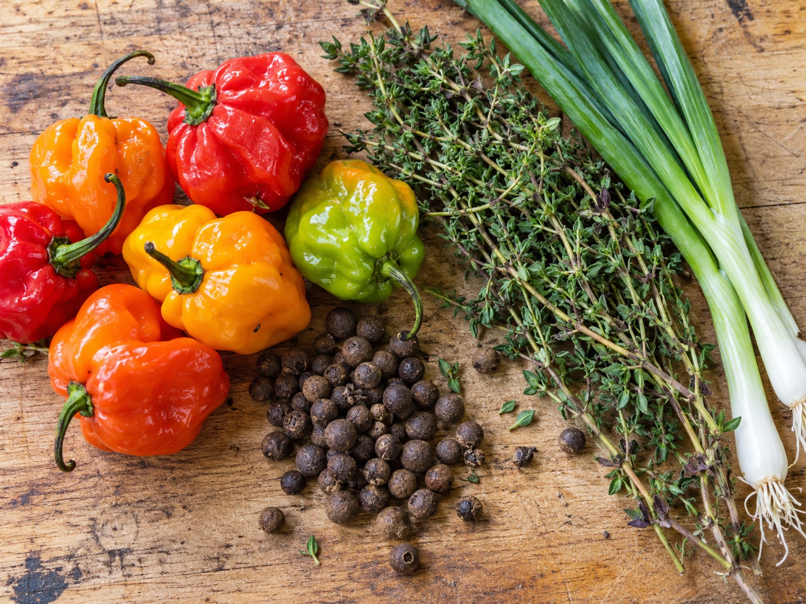 Scotch bonnet peppers, allspice berries, fresh thyme and scallions laid out on a wooden board