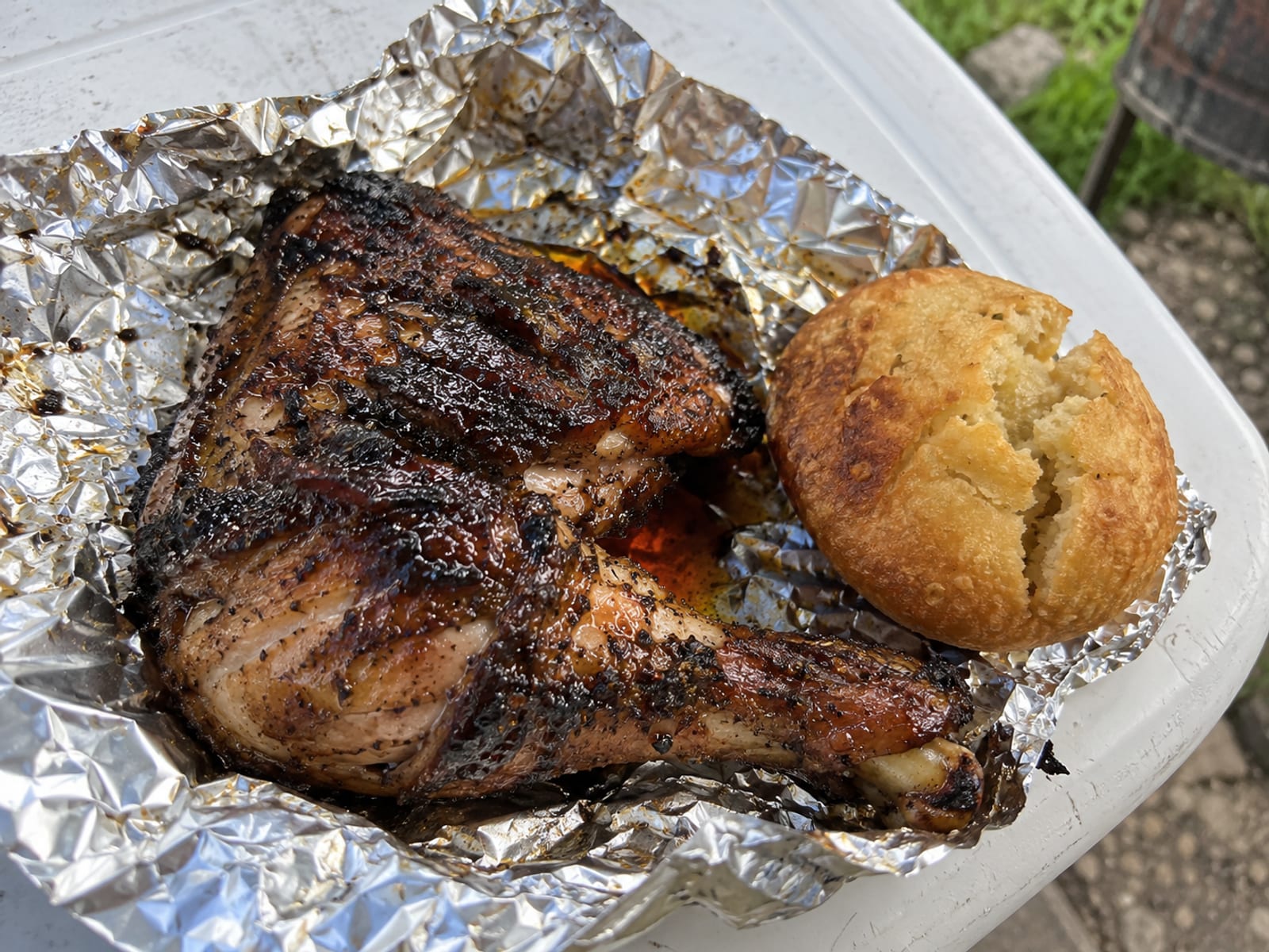 A jerk chicken quarter with dark crisp skin on foil beside a fried dumpling