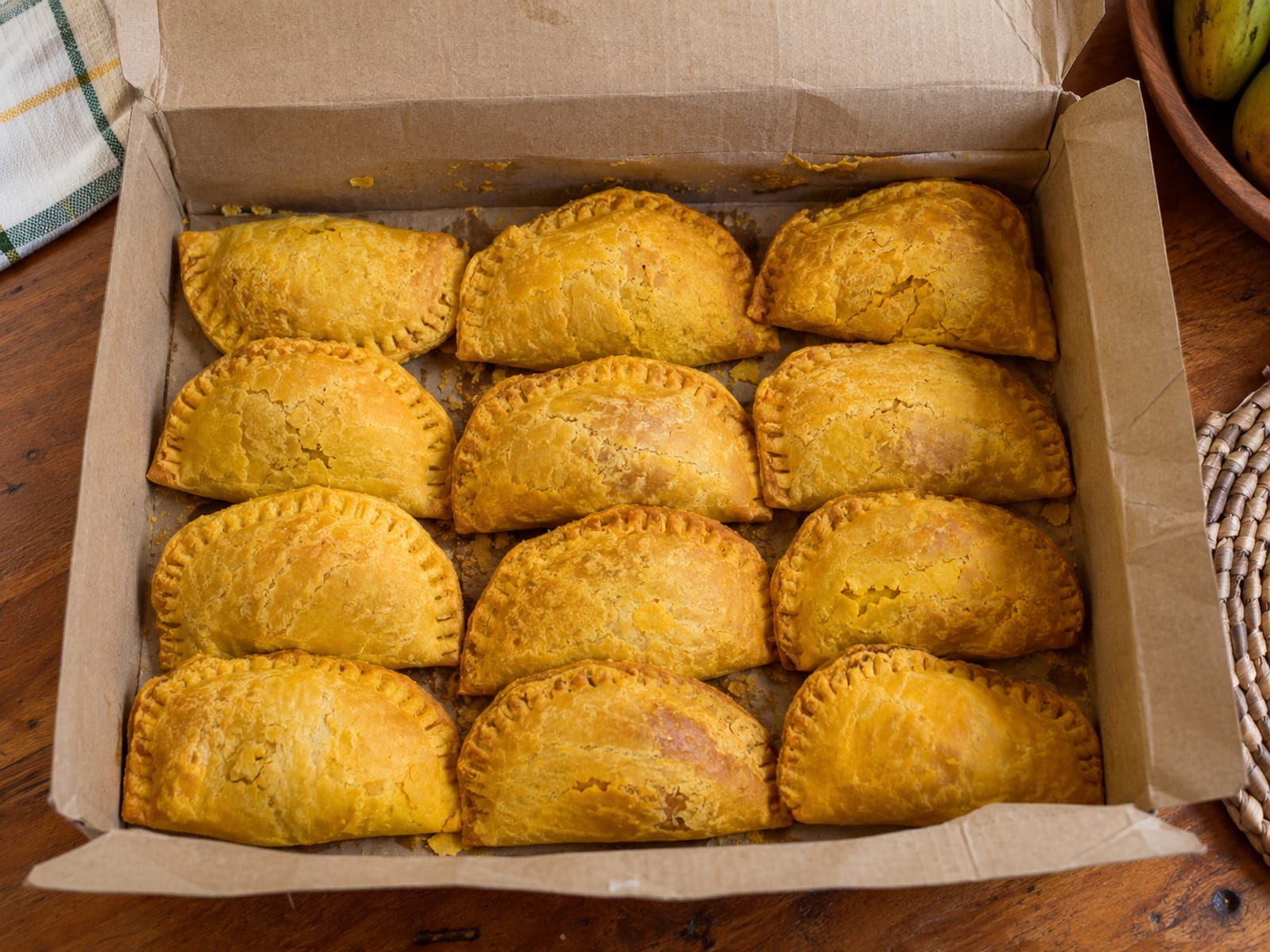 An open plain cardboard box holding a dozen golden patties on a kitchen table