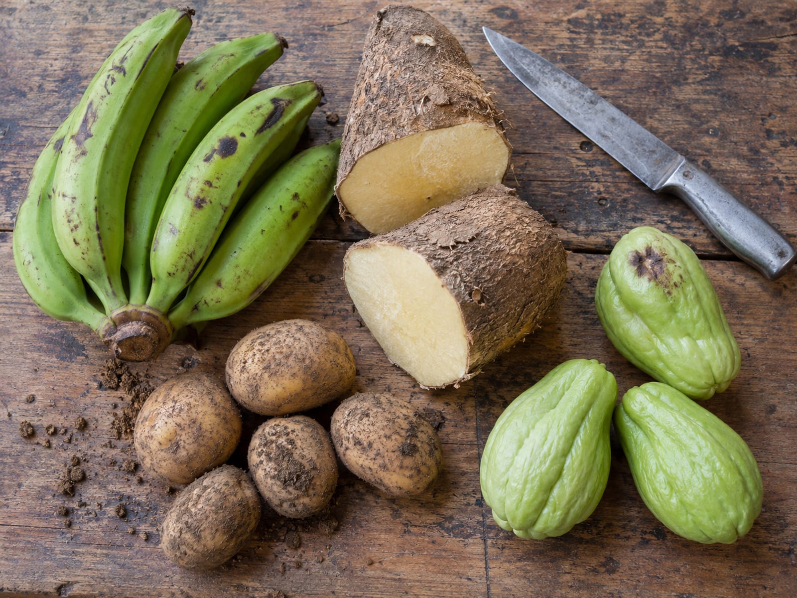 Green bananas, yellow yam, Irish potatoes and cho-cho laid out on a wooden table