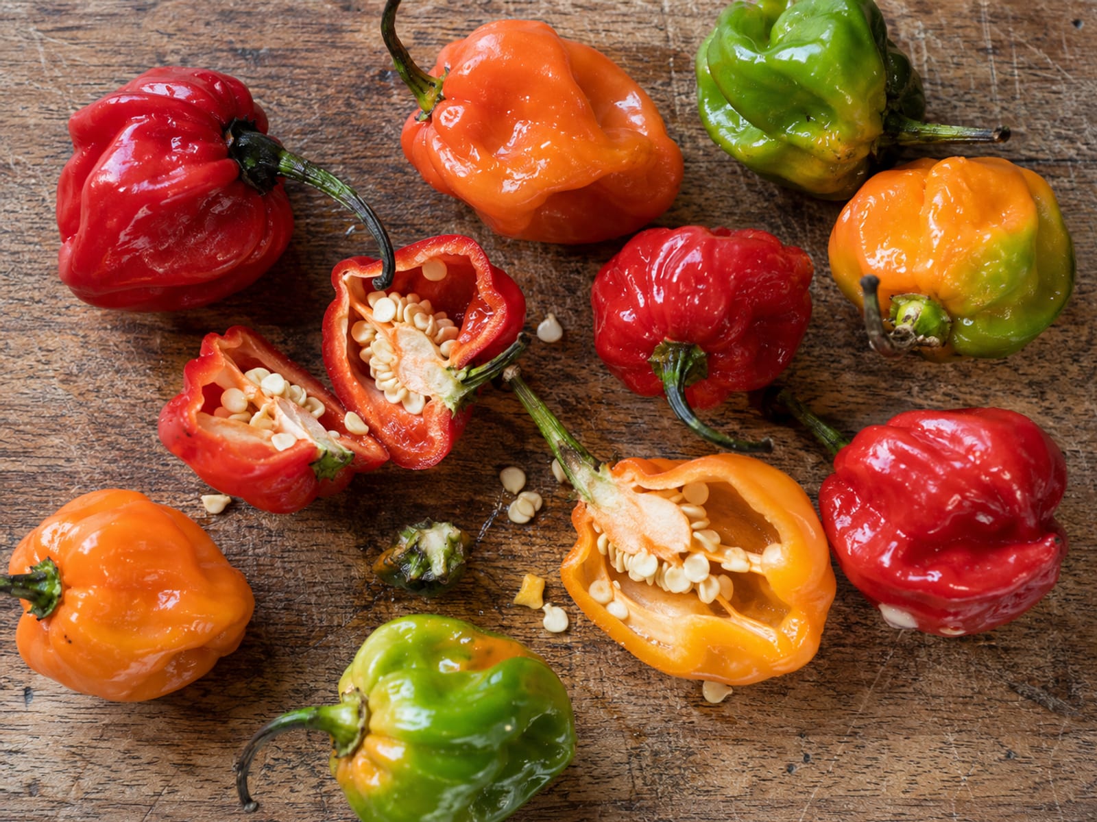 Red and green Scotch bonnet peppers on a wooden board