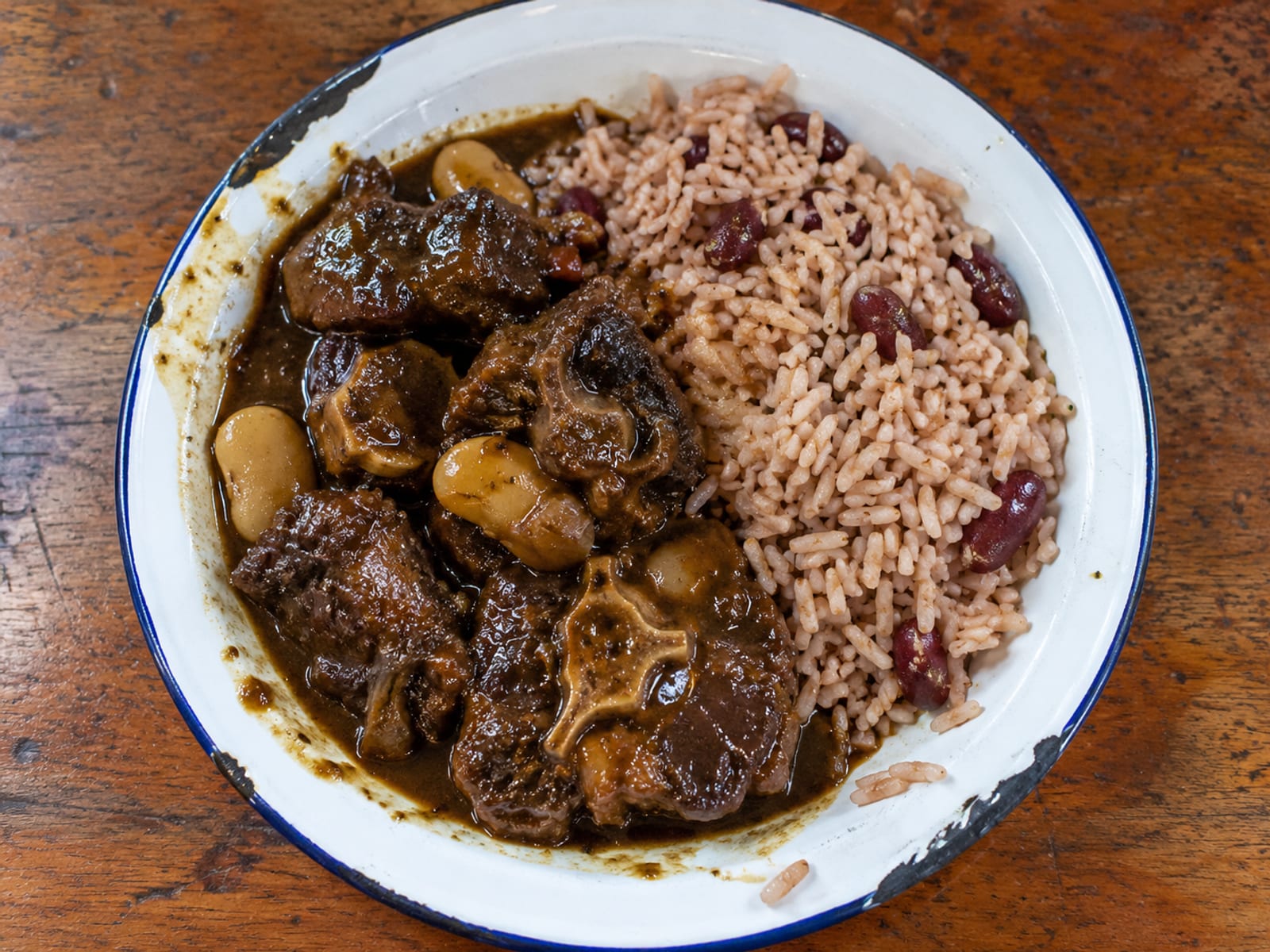 Braised oxtail in dark gravy with butter beans beside rice and peas