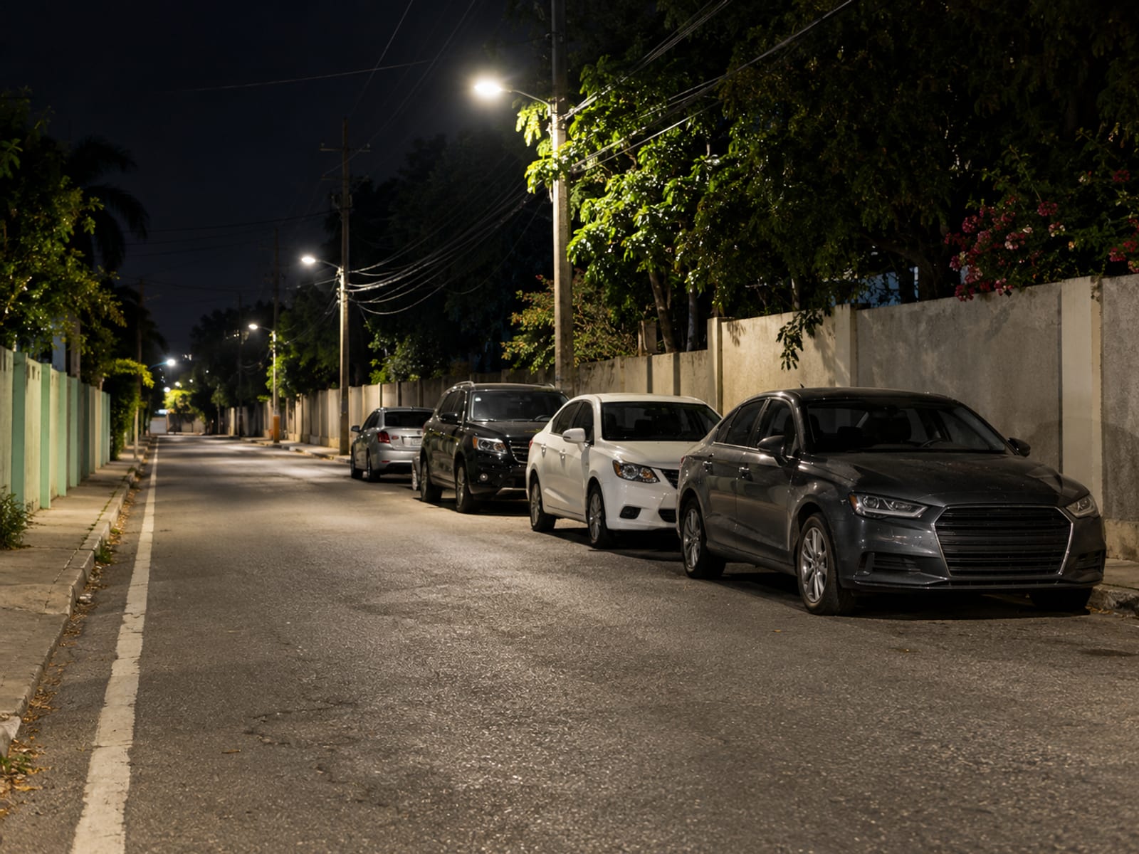 A lit street at night with cars parked neatly off to the side of the road