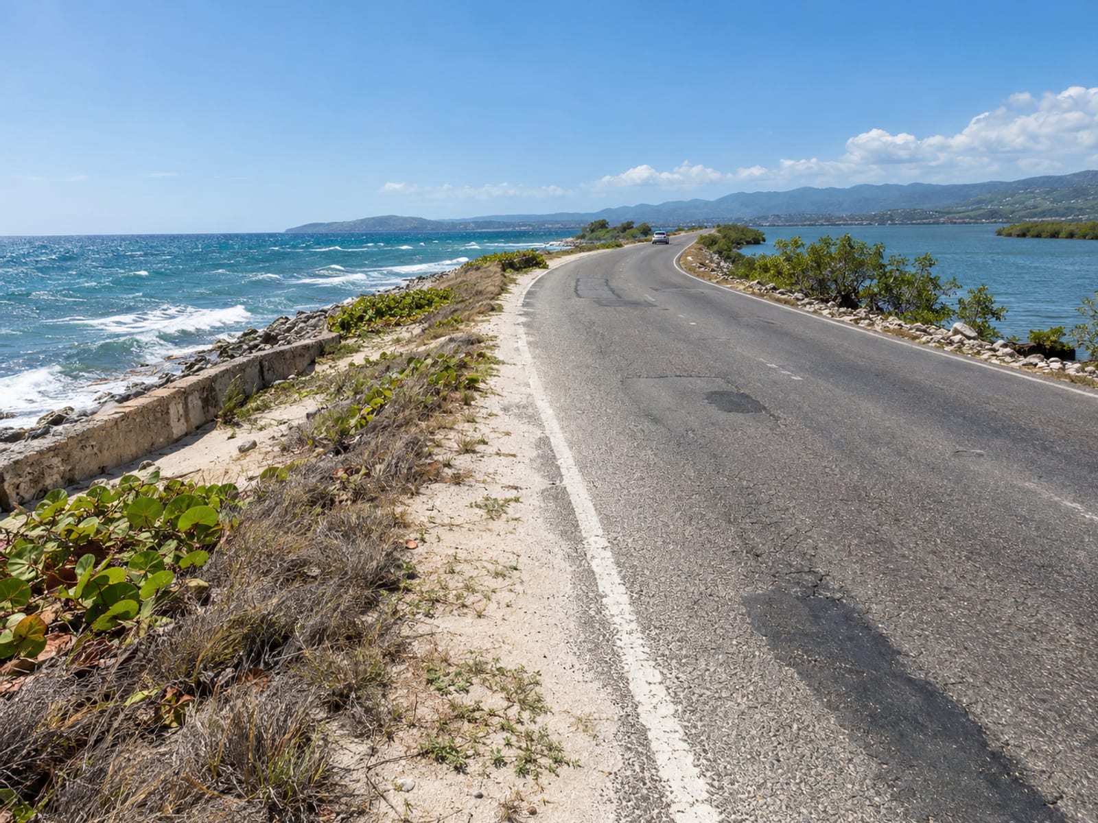 A coastal road with the Caribbean Sea on one side and a harbour on the other
