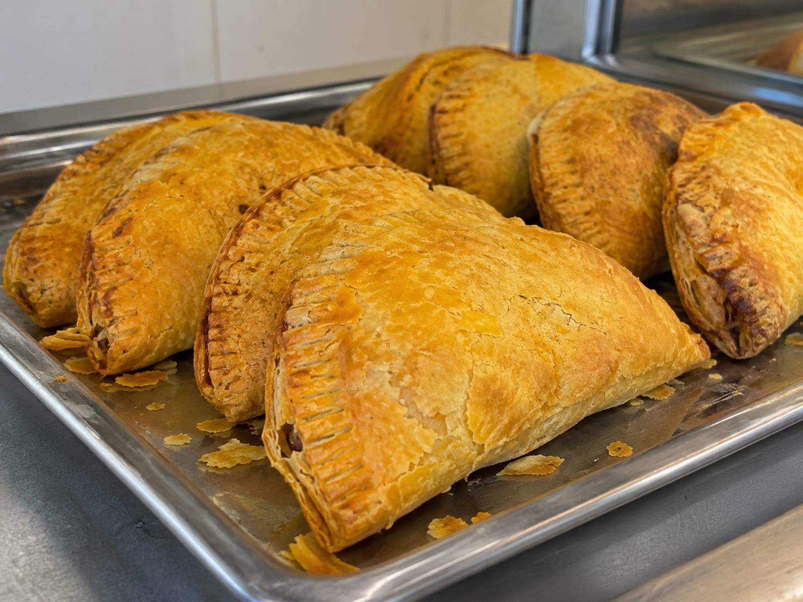 Golden Jamaican beef patties on a plain metal tray on a counter