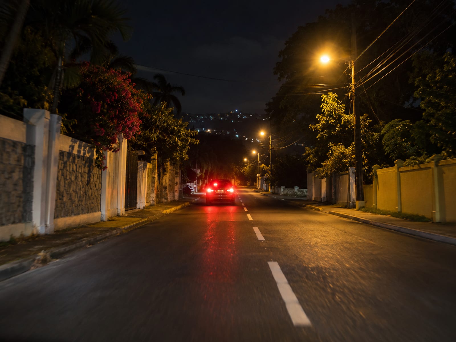 A quiet lit road at night with the tail lights of a car