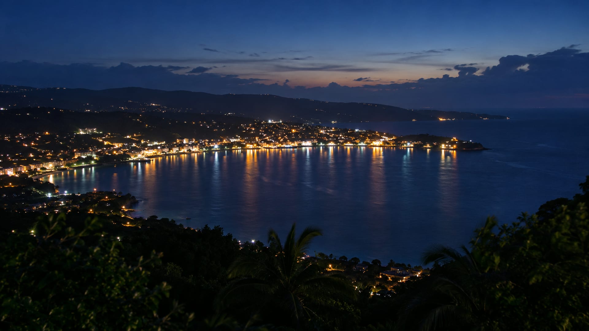 A curved bay at night with town lights reflected on calm dark water