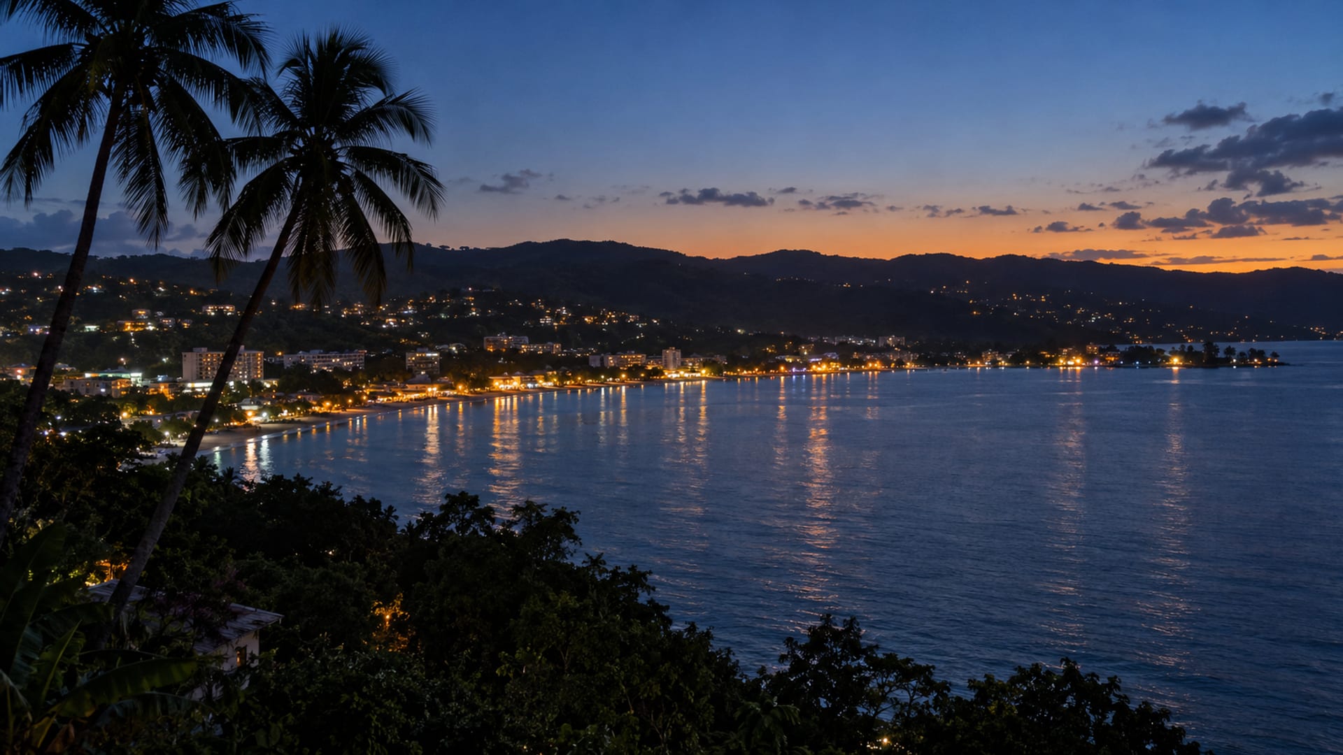 Warm lights along a curved tropical coastline at dusk with a calm dark sea