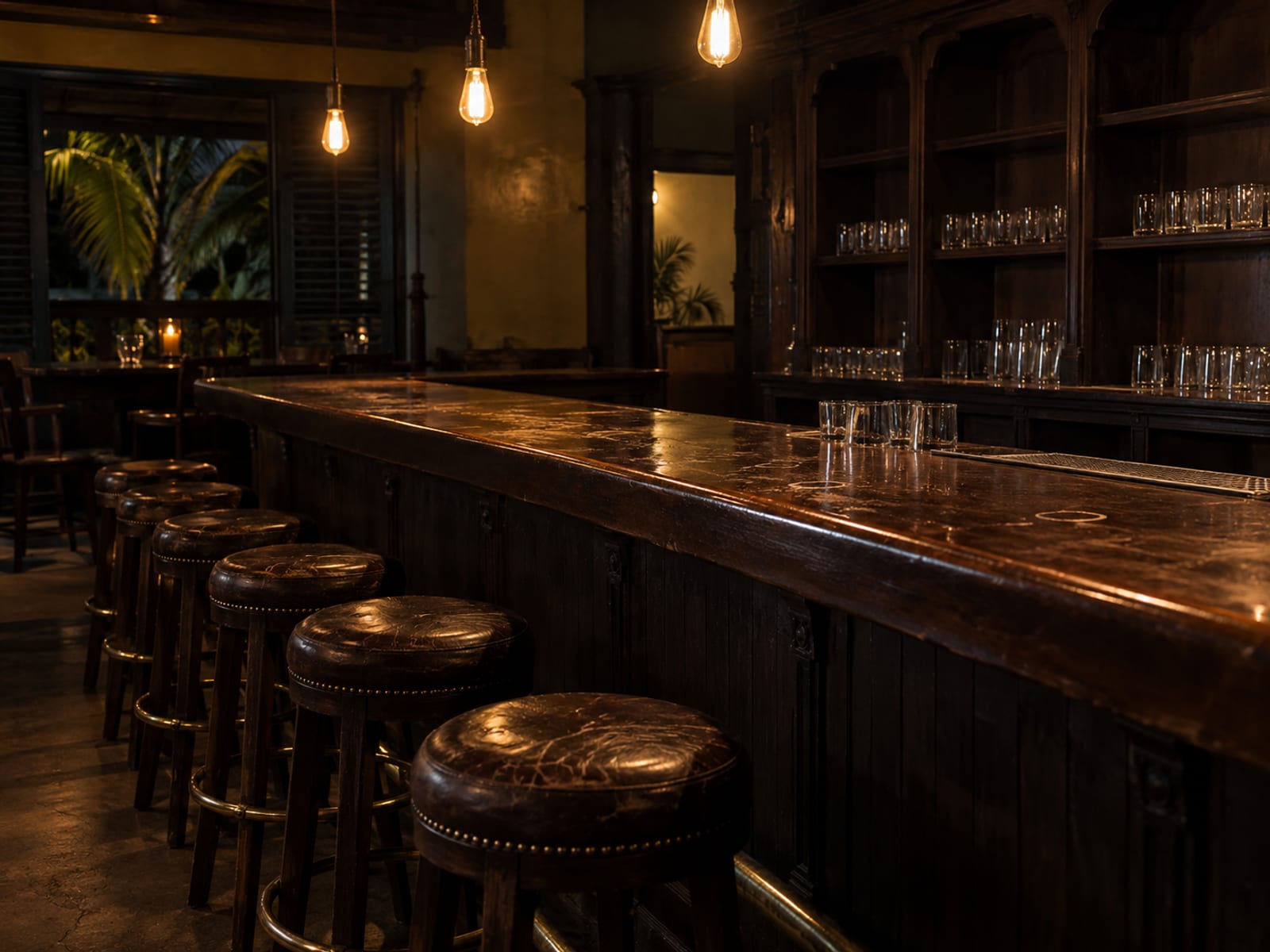 A dim bar counter with empty stools and warm hanging lights