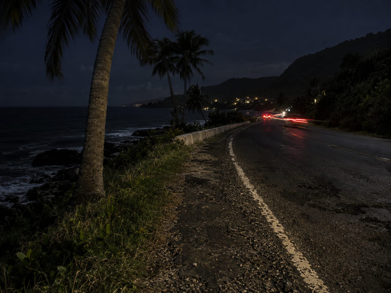 A coastal road at night with red taillights blurred in the distance