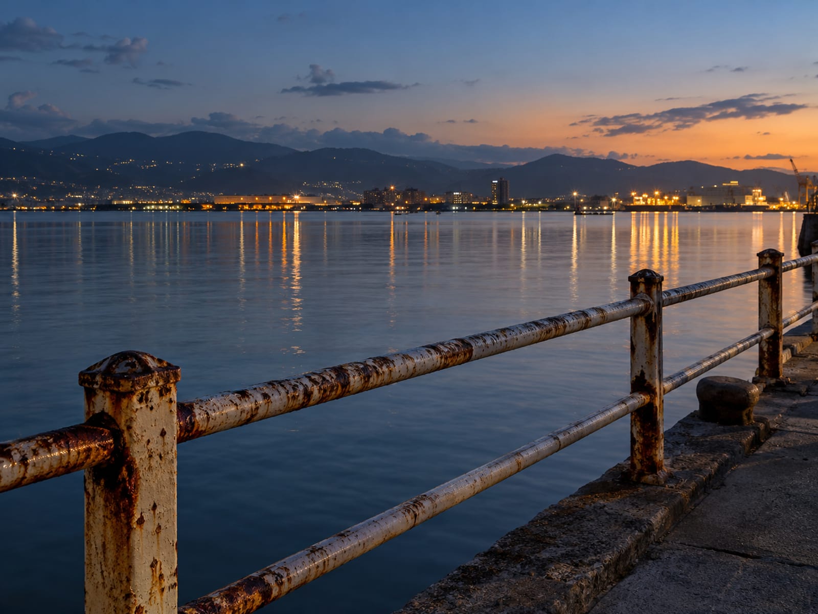 Kingston harbour at dusk with calm water and lights along the shore
