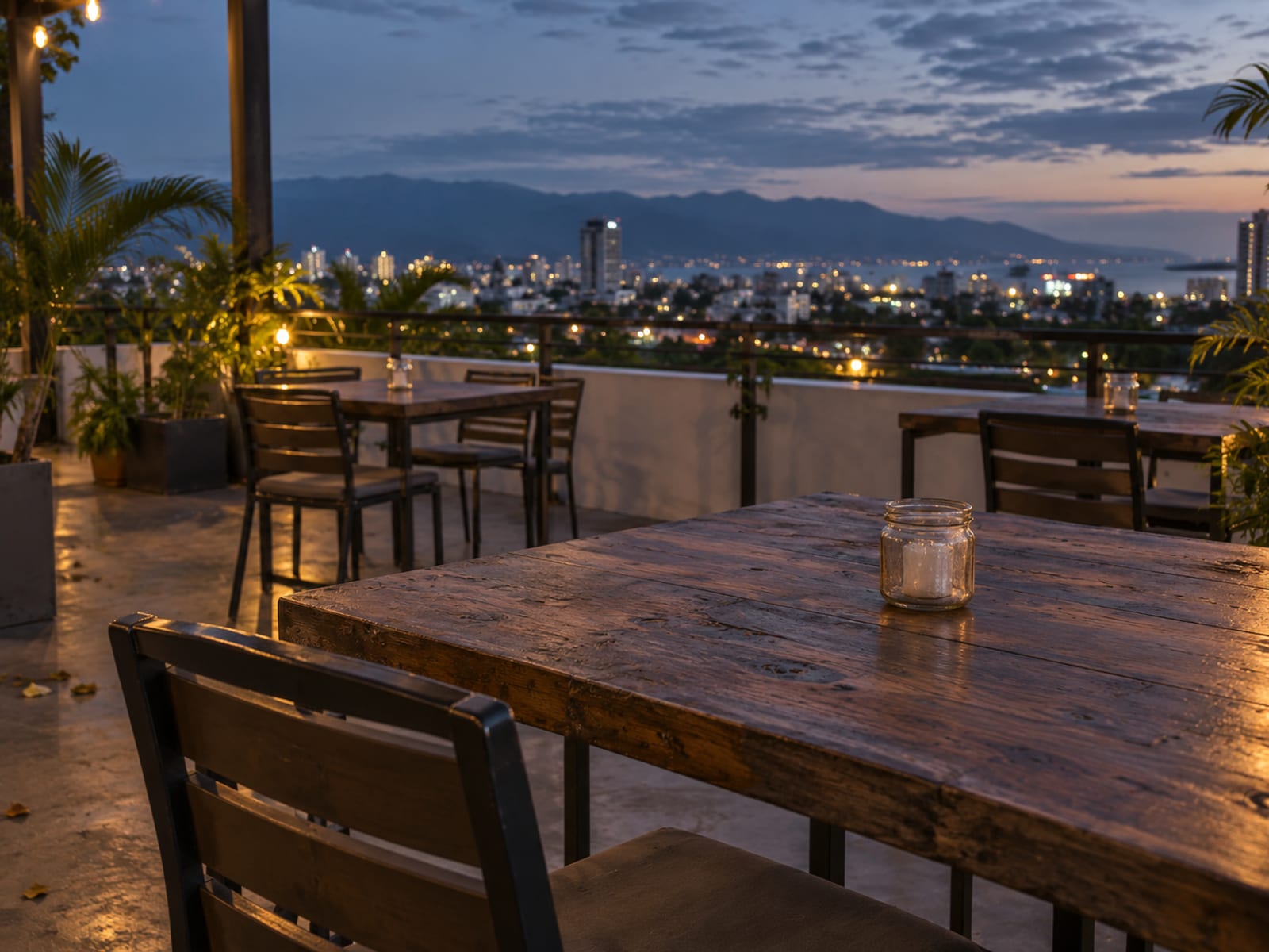 Empty open-air rooftop terrace tables at dusk with city lights beyond