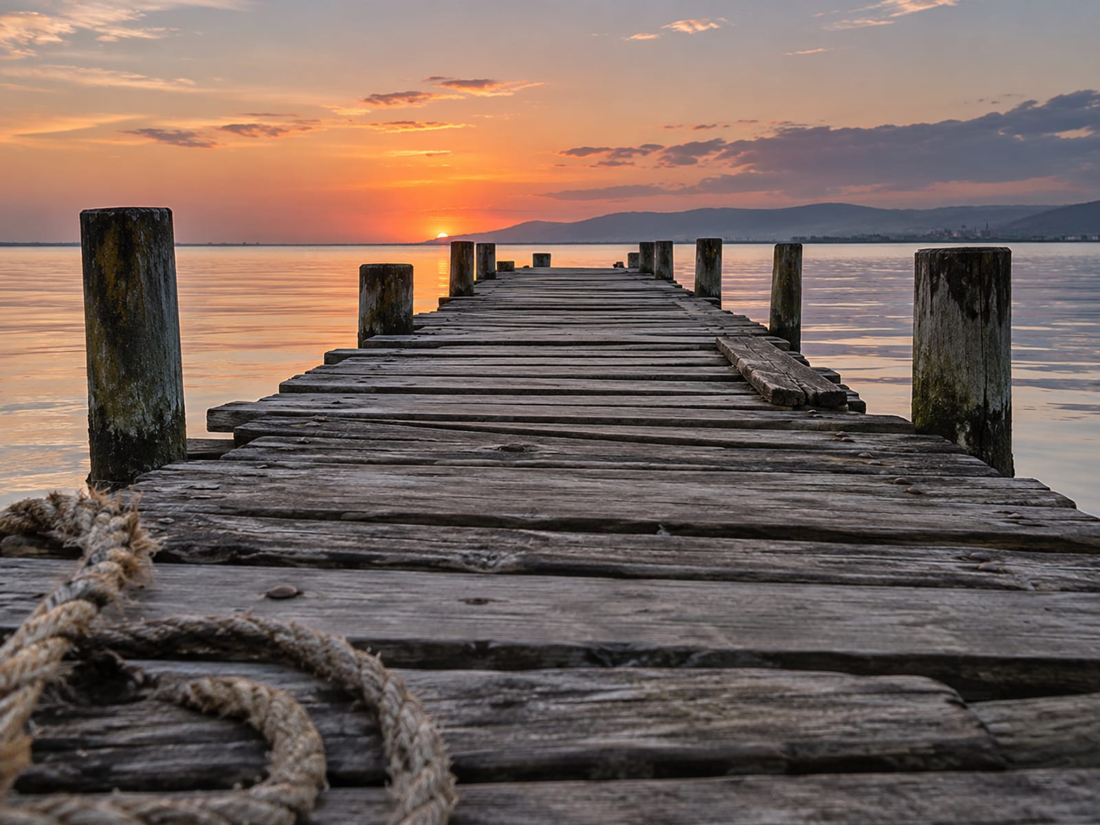 Wooden pier extending over calm harbour water at sunset