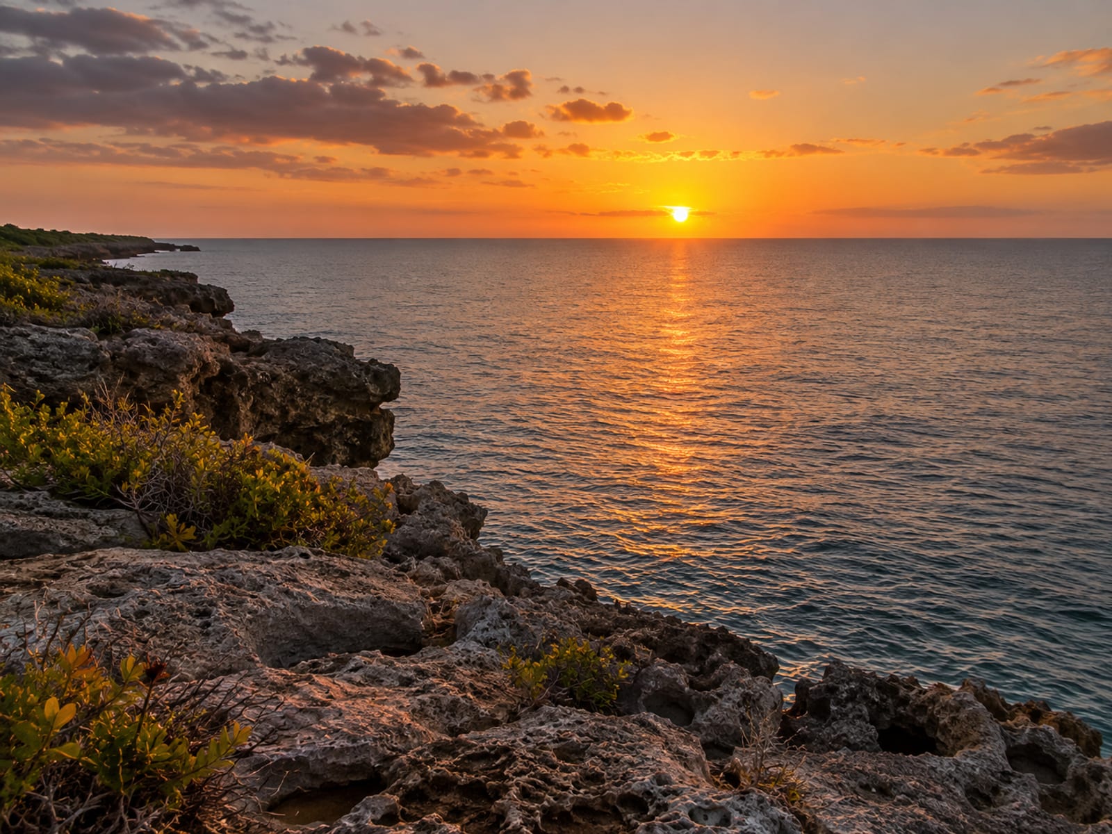 Sunset over calm turquoise sea seen from a rocky cliff edge