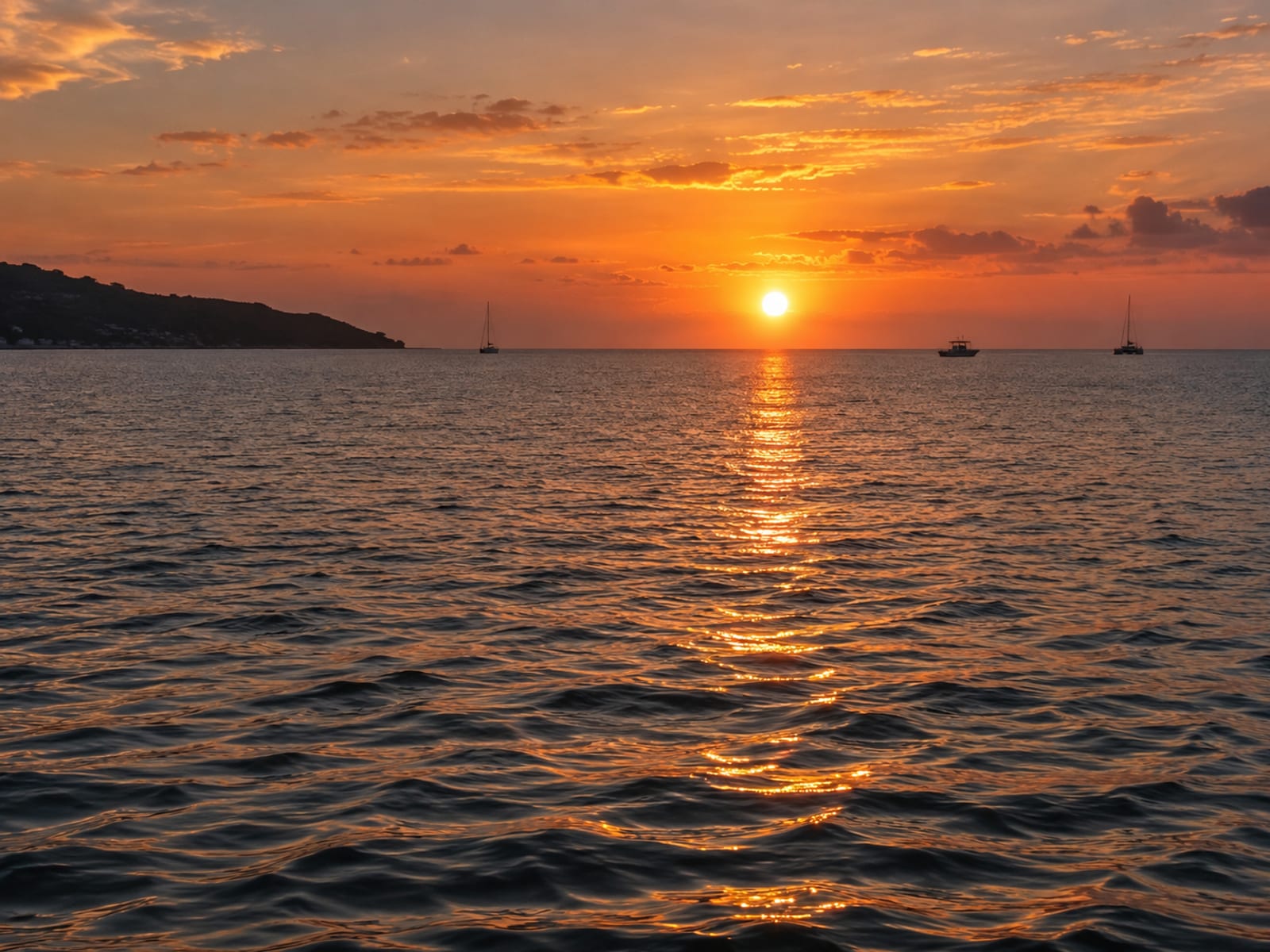 The sun low over a calm bay with an orange sky and a few small boats