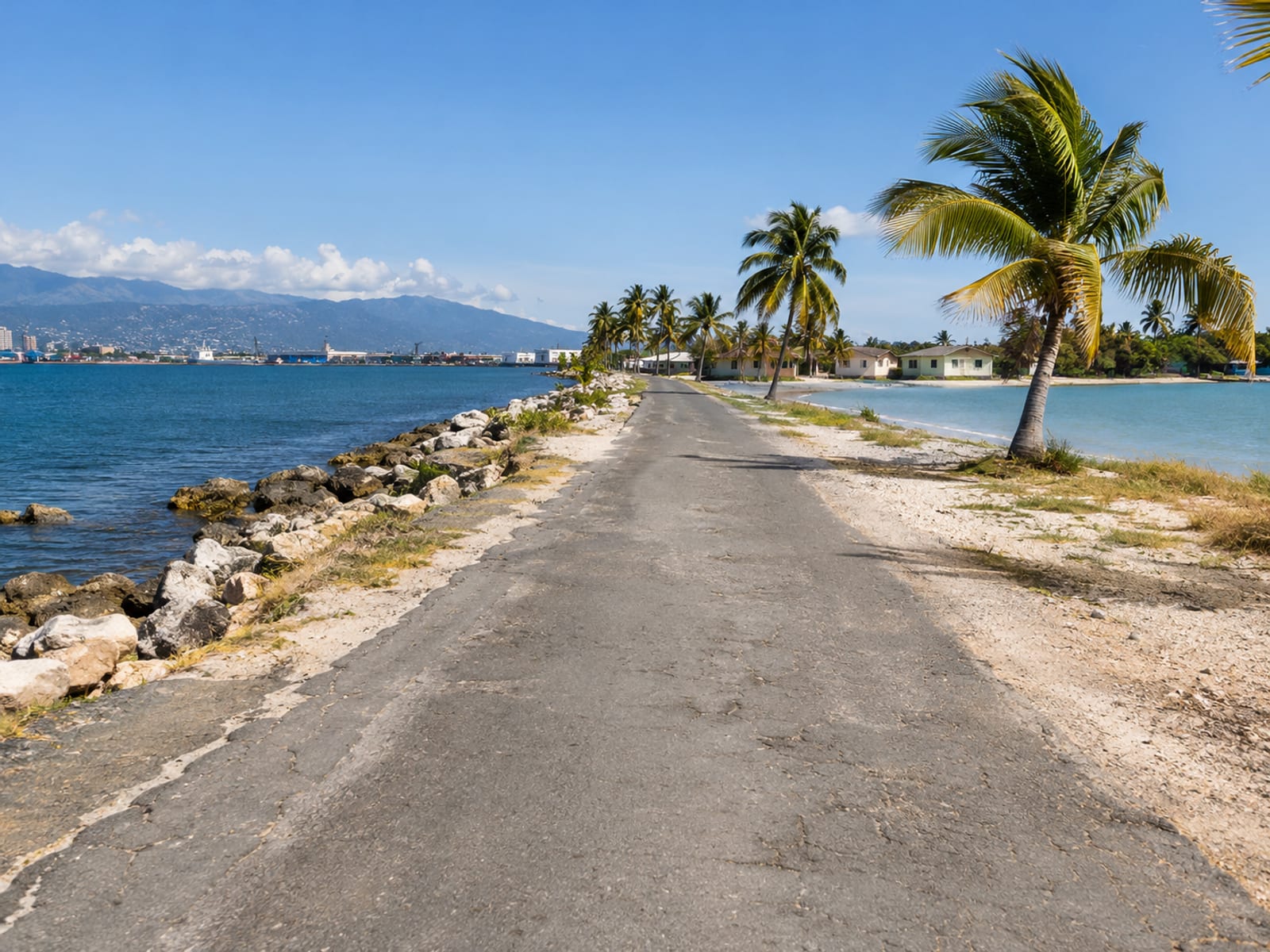 A narrow coastal road running along the harbour toward Port Royal under a clear sky