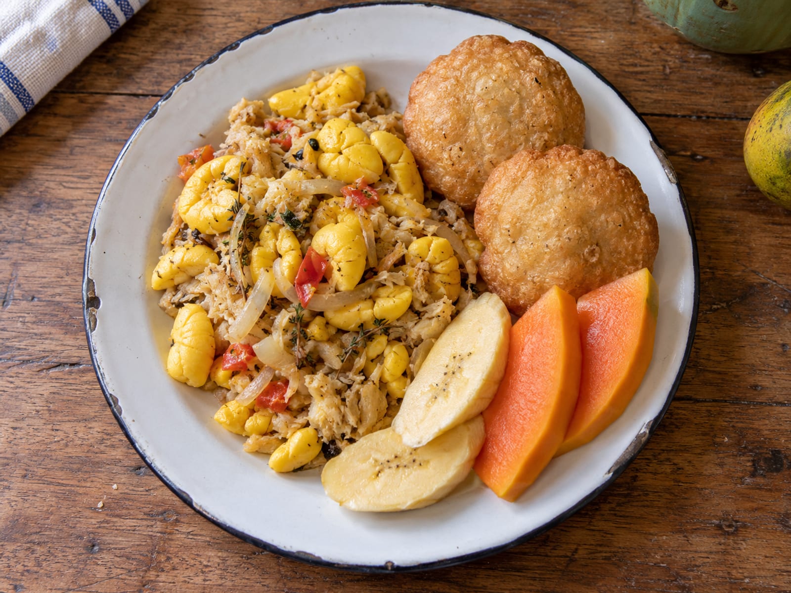A Jamaican breakfast plate with fried dumplings and fresh fruit on a wooden table