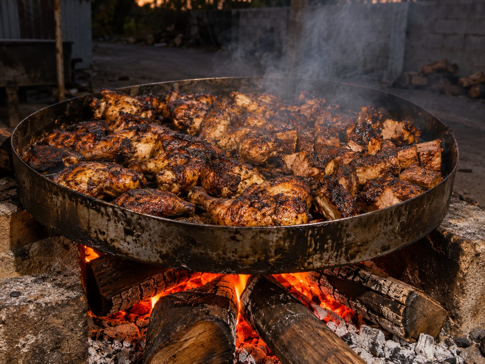 A jerk pan of chicken and pork smoking over pimento wood logs