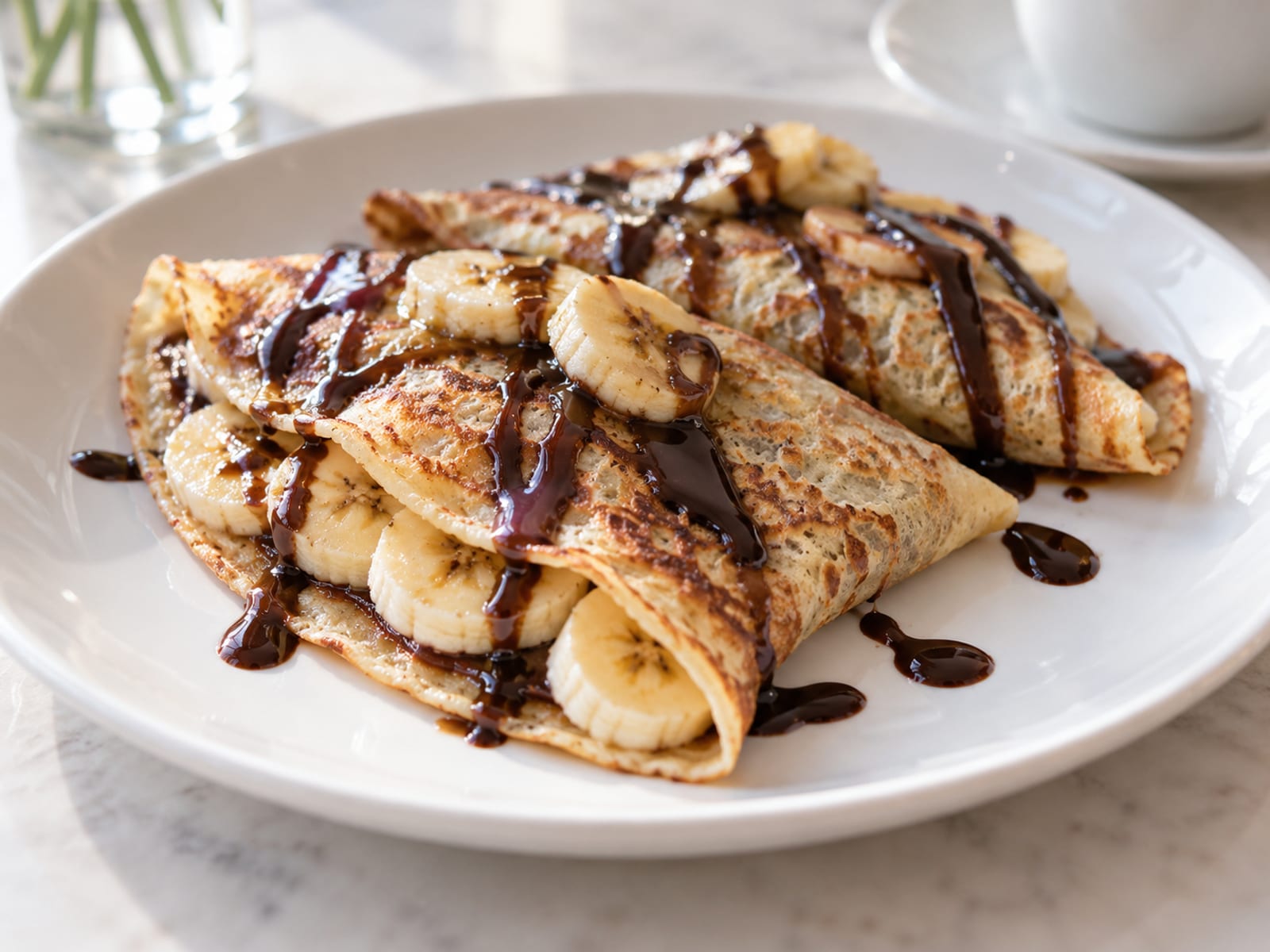 Two folded crêpes with sliced banana and chocolate sauce on a white plate
