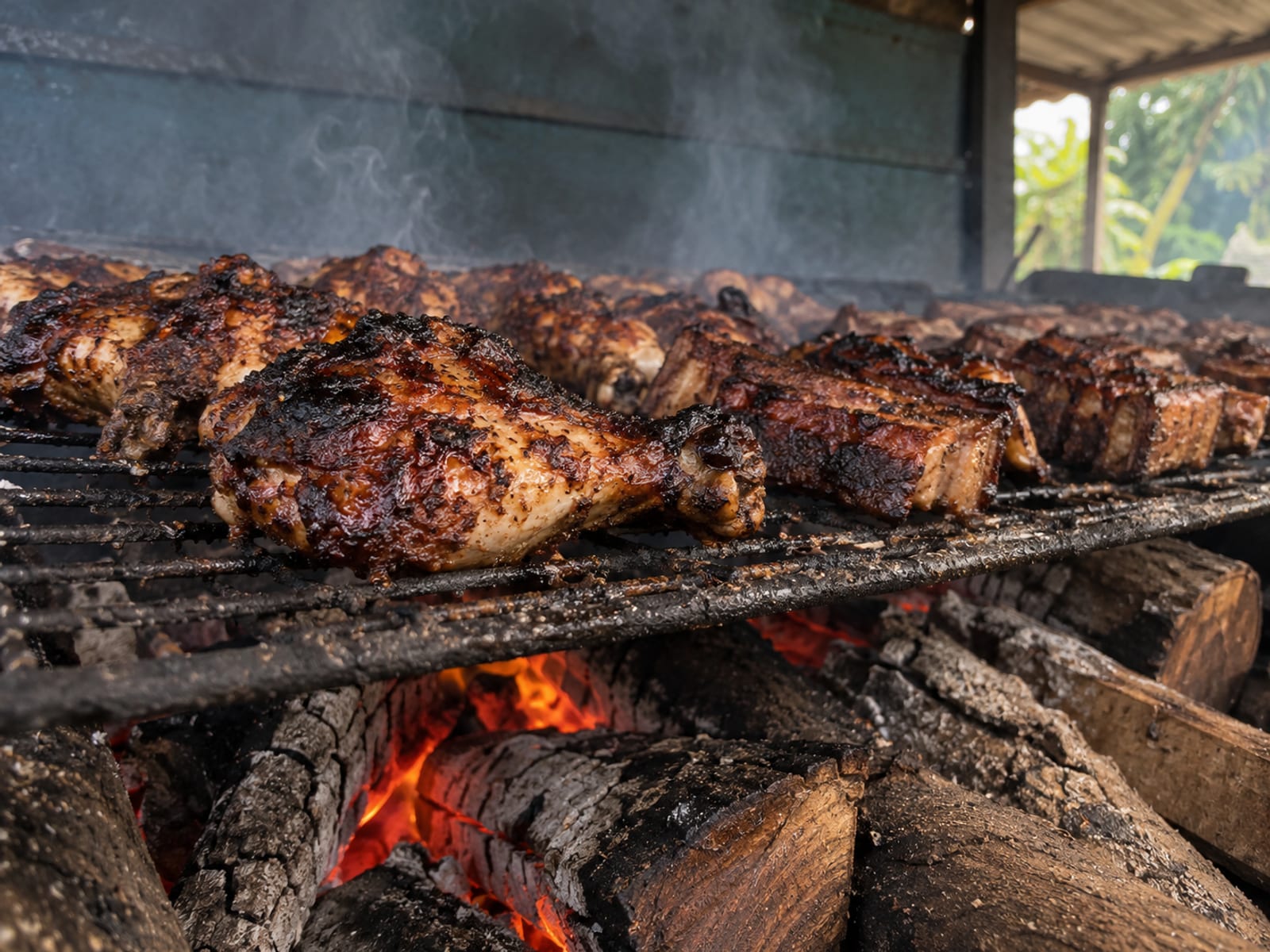 Jerk chicken and pork smoking on a grill over glowing pimento wood coals